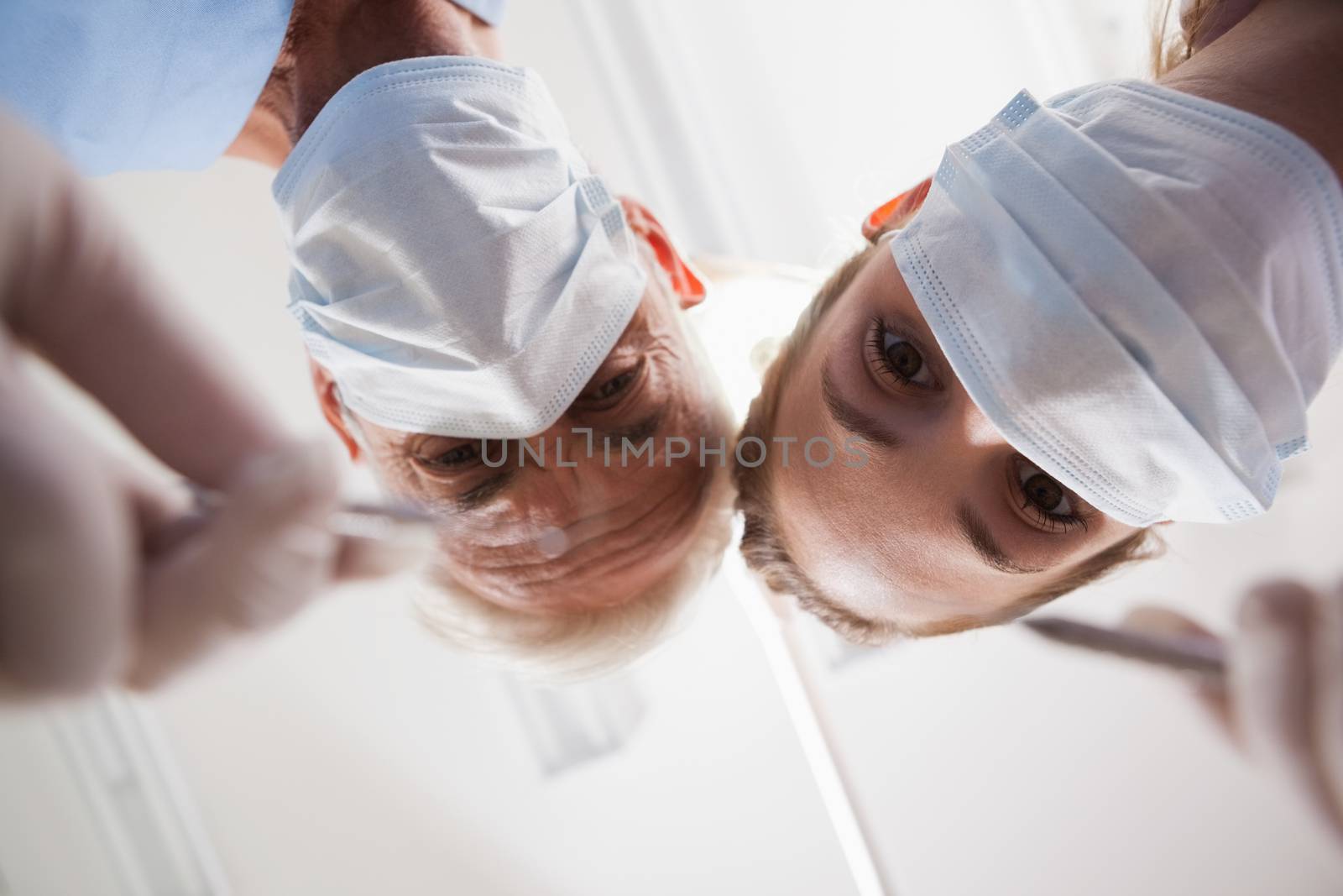 Dentist and assistant leaning over patient with tools by Wavebreakmedia