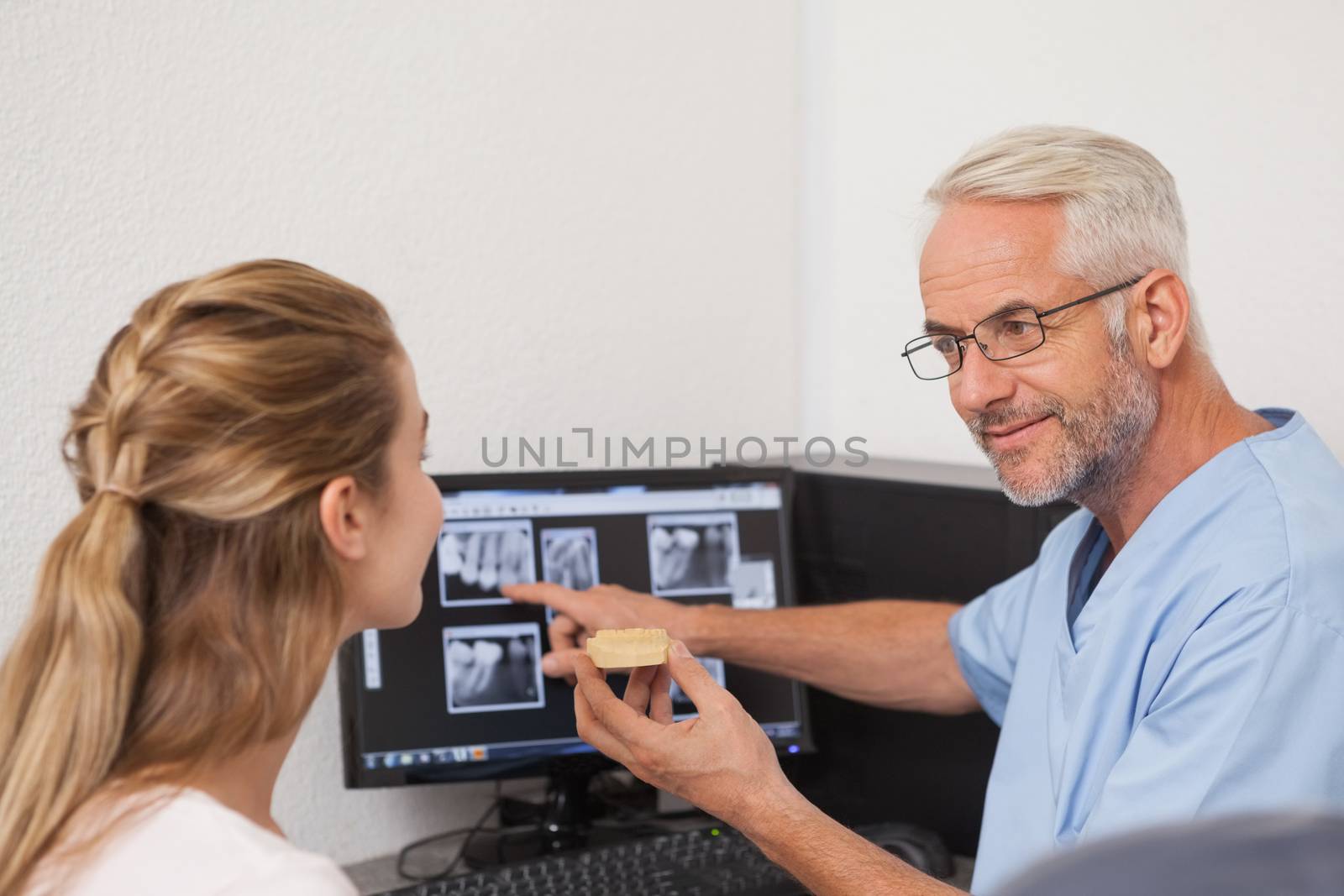 Dentist showing patient model of teeth and xrays by Wavebreakmedia
