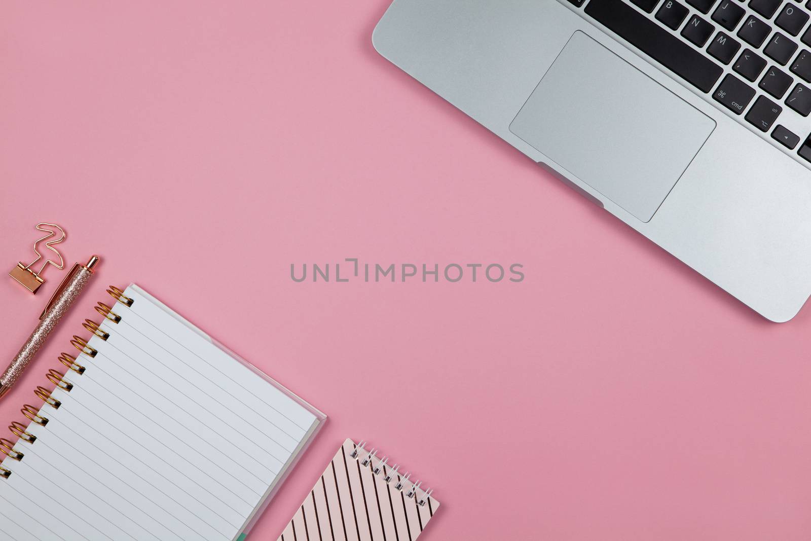 Modern female working space, top view. Laptop, notebooks, pen, clamp on pink backround, copy space, flat lay. Desktop of freelancer. Work from home concept. Horizontal.