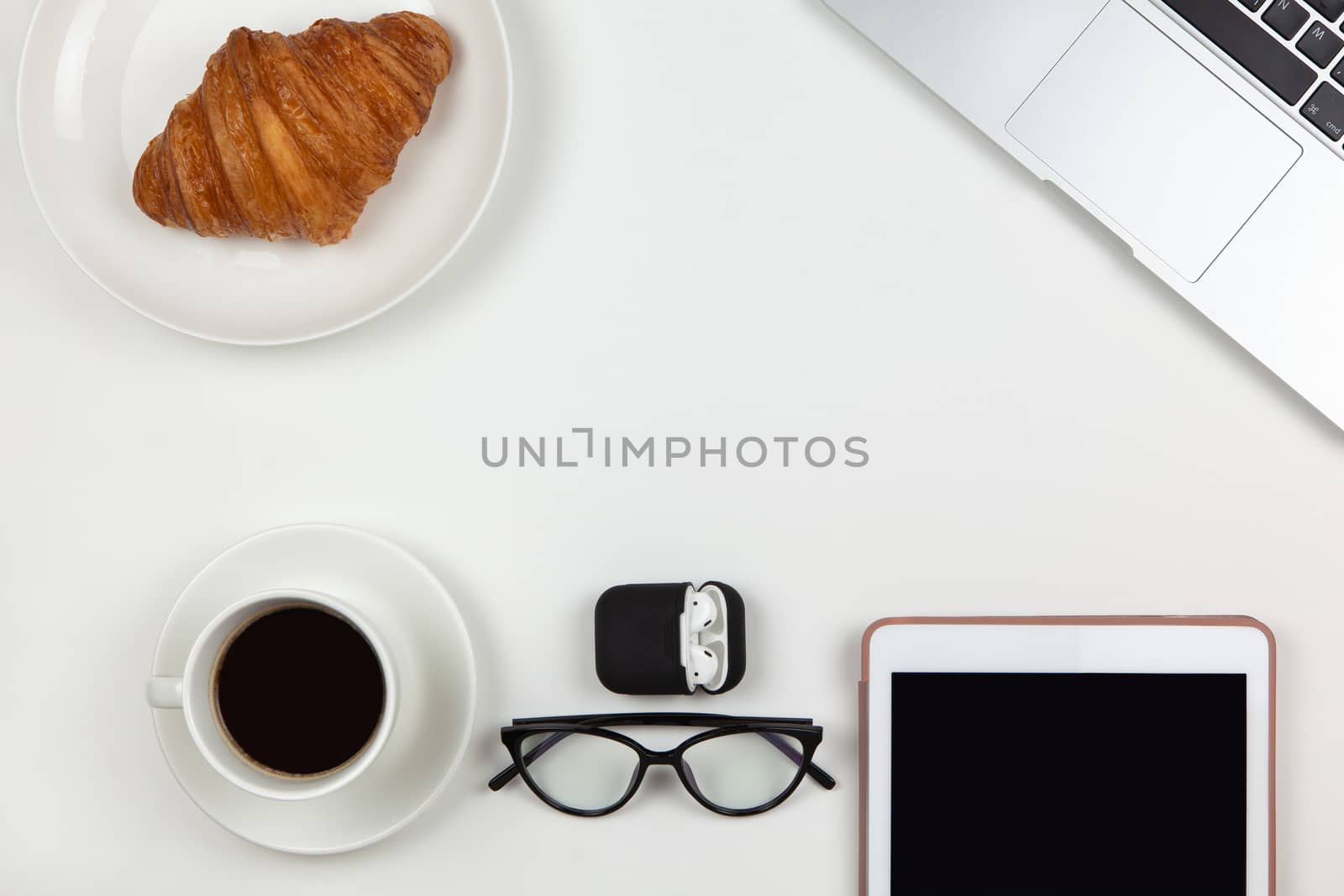 Business breakfast concept. Modern unisex working space, top view. Laptop, coffee, tablet, croissant, glasses, headphones in case on white background, copy space, flat lay. Desktop of freelancer.