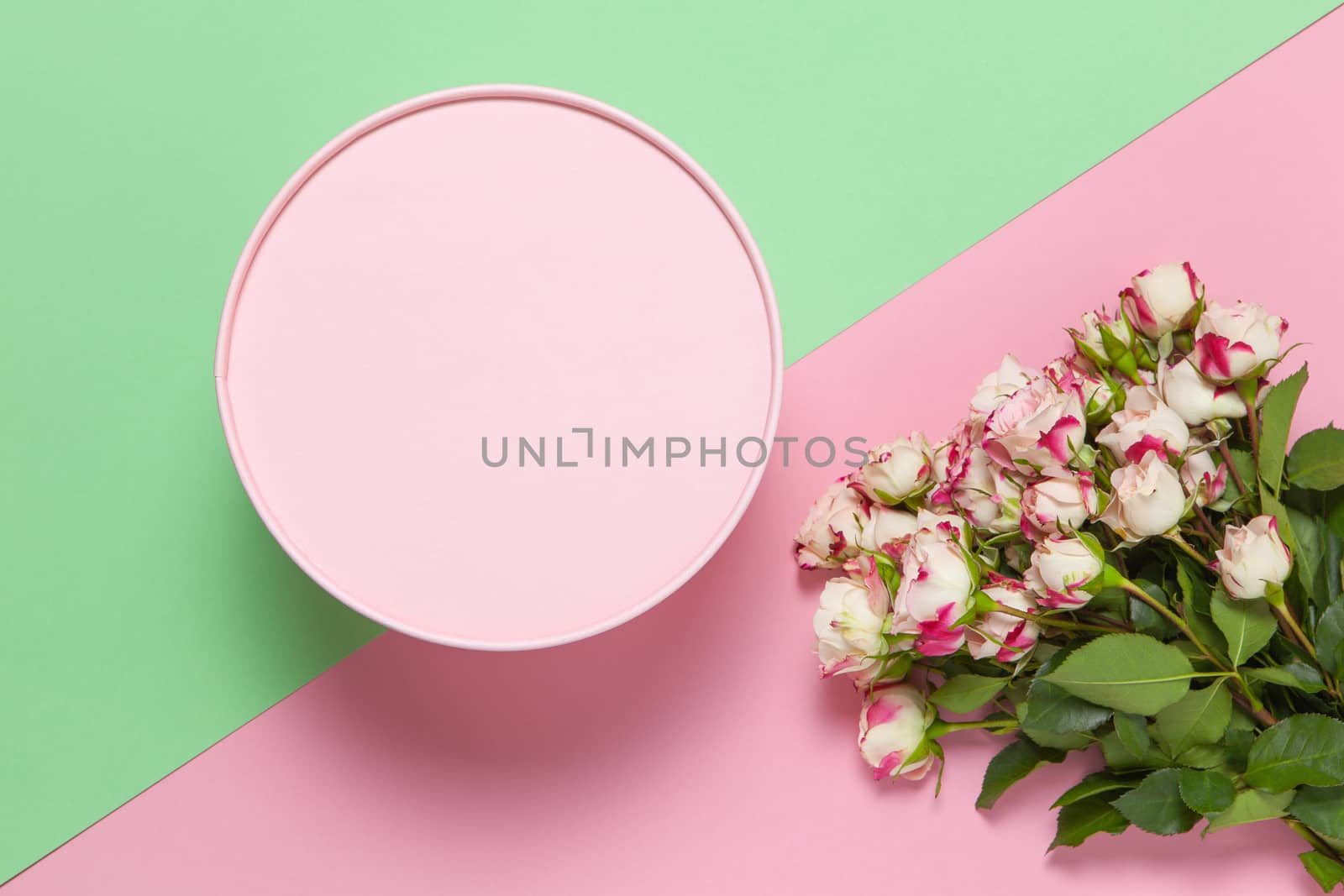 Pink round gift box, bouquet of small roses on pastel two-color background pink and green, copy space, flat lay. March 8, February 14, St. Valentine's, Mother's, Women's day celebration concept.