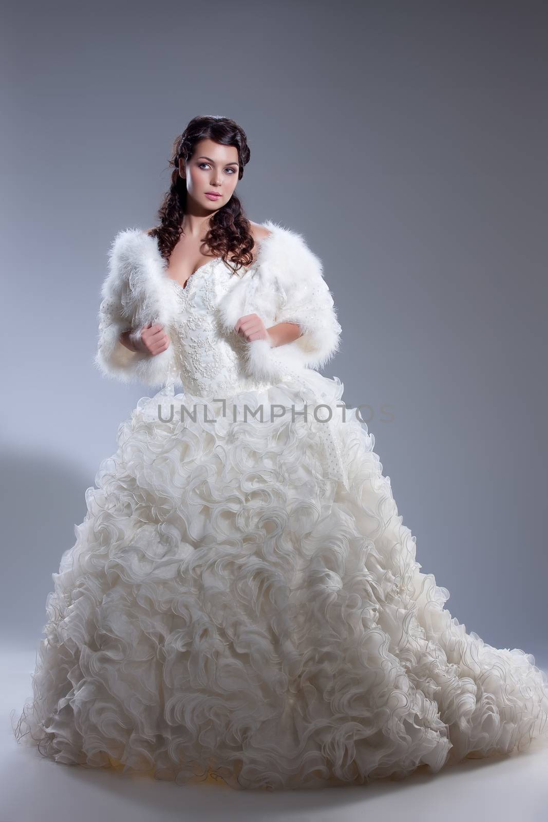 Young beautiful brunette in fashionable wedding dress on isolated studio background