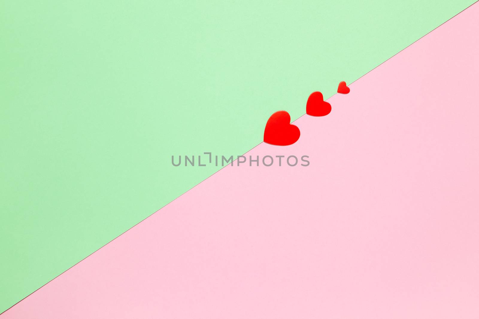 Festive spring flat lay. Three red hearts on pastel two-color background pink and green, copy space. March 8, February 14, Birthday, St. Valentine's, Mother's, Women's day celebration concept.