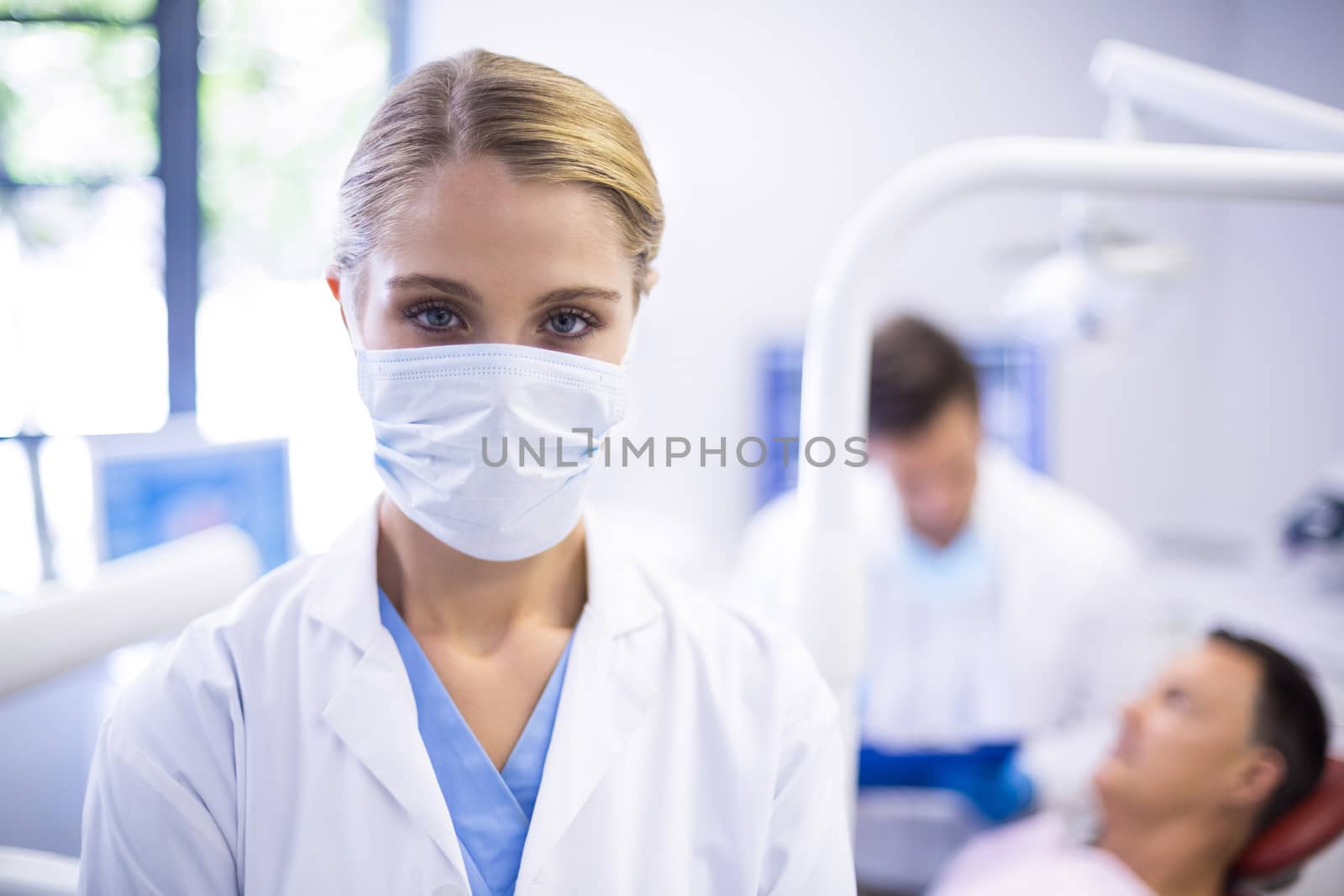 Portrait of dentist wearing surgical mask while her colleague examining patient in background