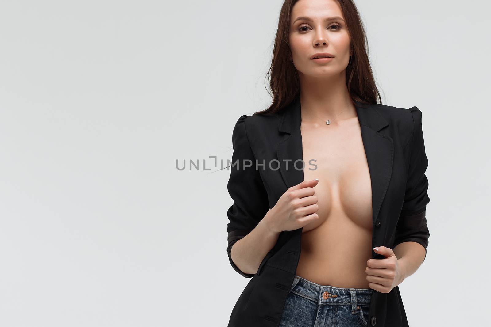 Long haired relaxed brunette woman with naked breast in black suit provocatively looking at camera