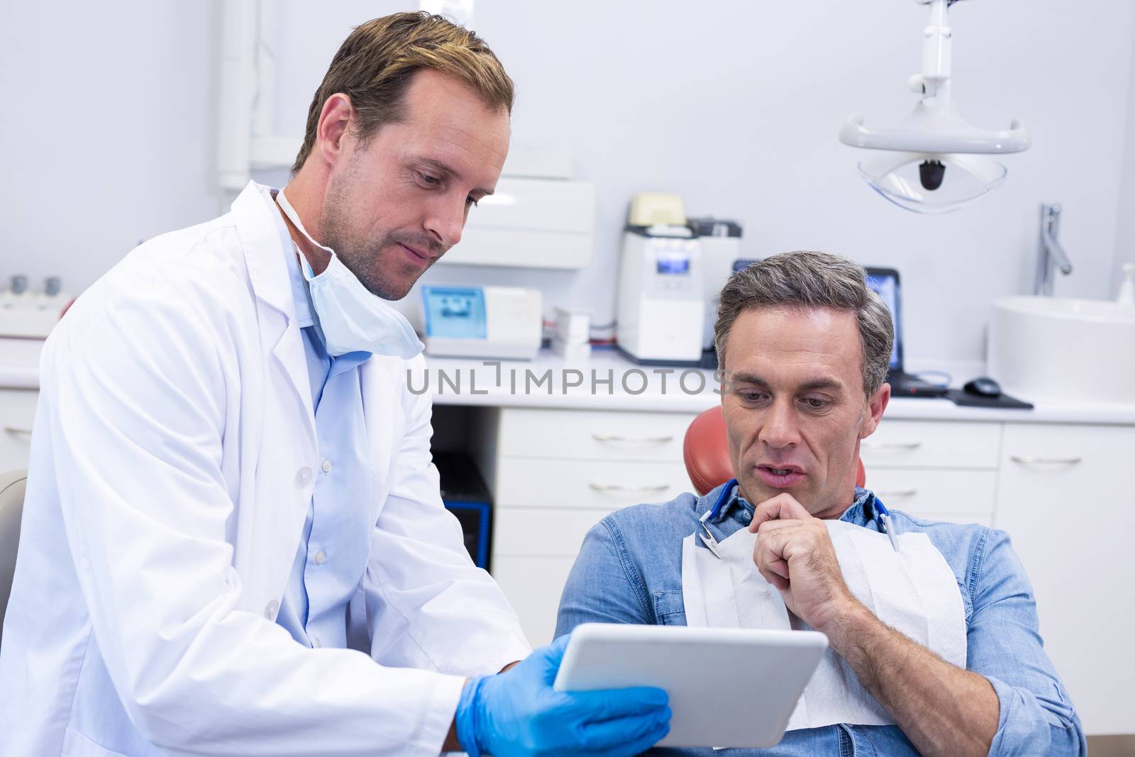 Dentist discussing over digital tablet with male patient by Wavebreakmedia