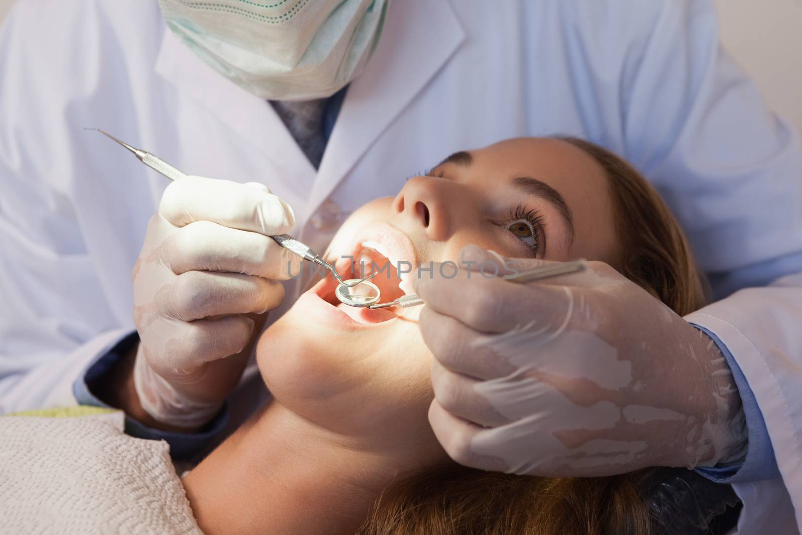 Dentist examining a patients teeth in the dentists chair under bright light by Wavebreakmedia