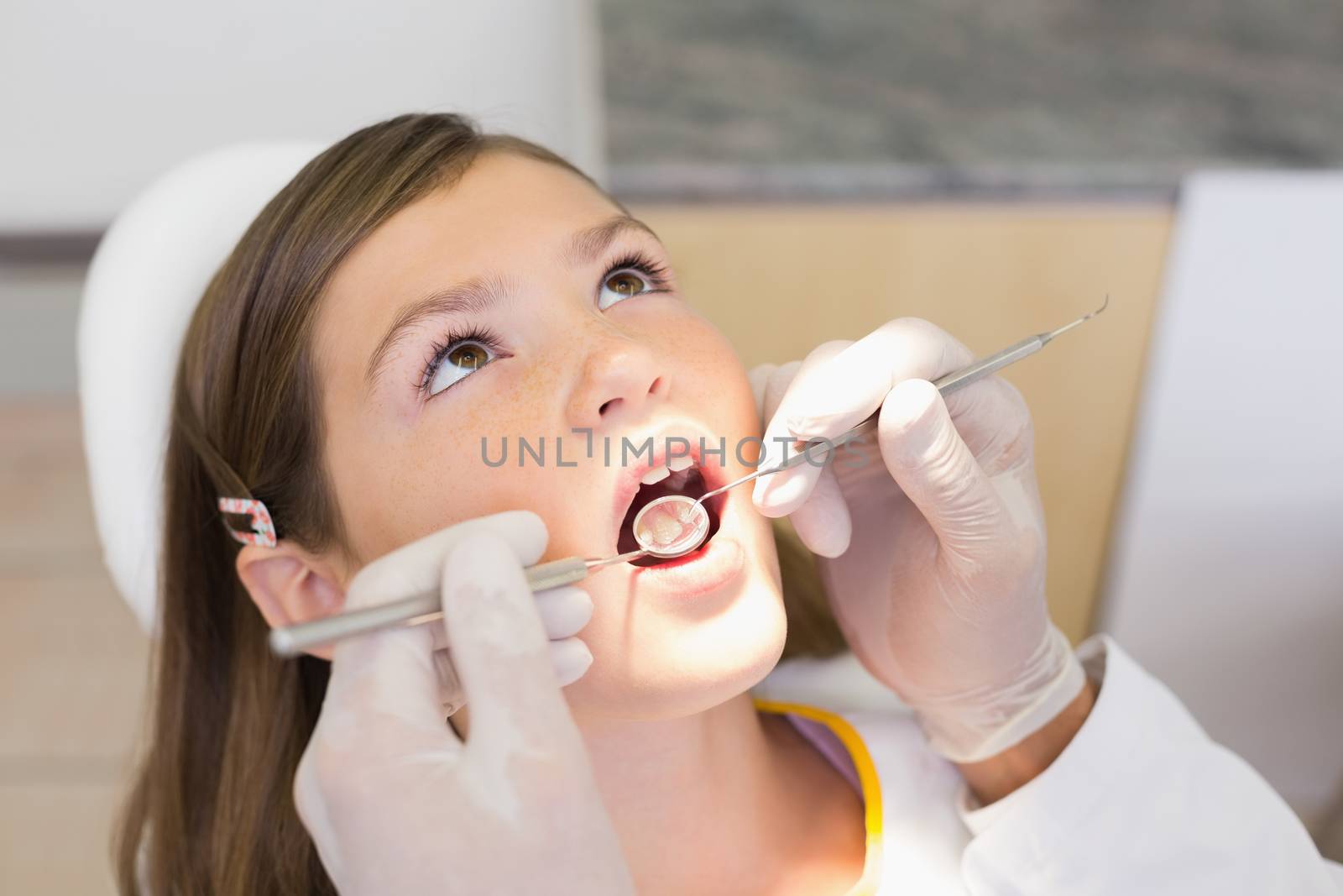 Pediatric dentist examining a little girls teeth in the dentists chair by Wavebreakmedia