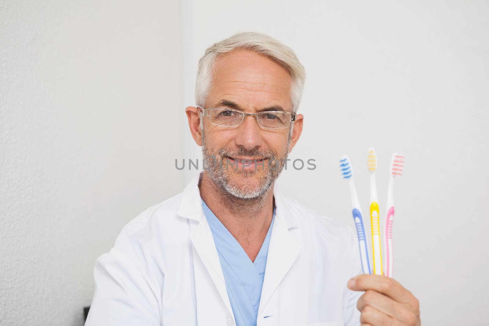 Dentist smiling at camera holding toothbrushes by Wavebreakmedia