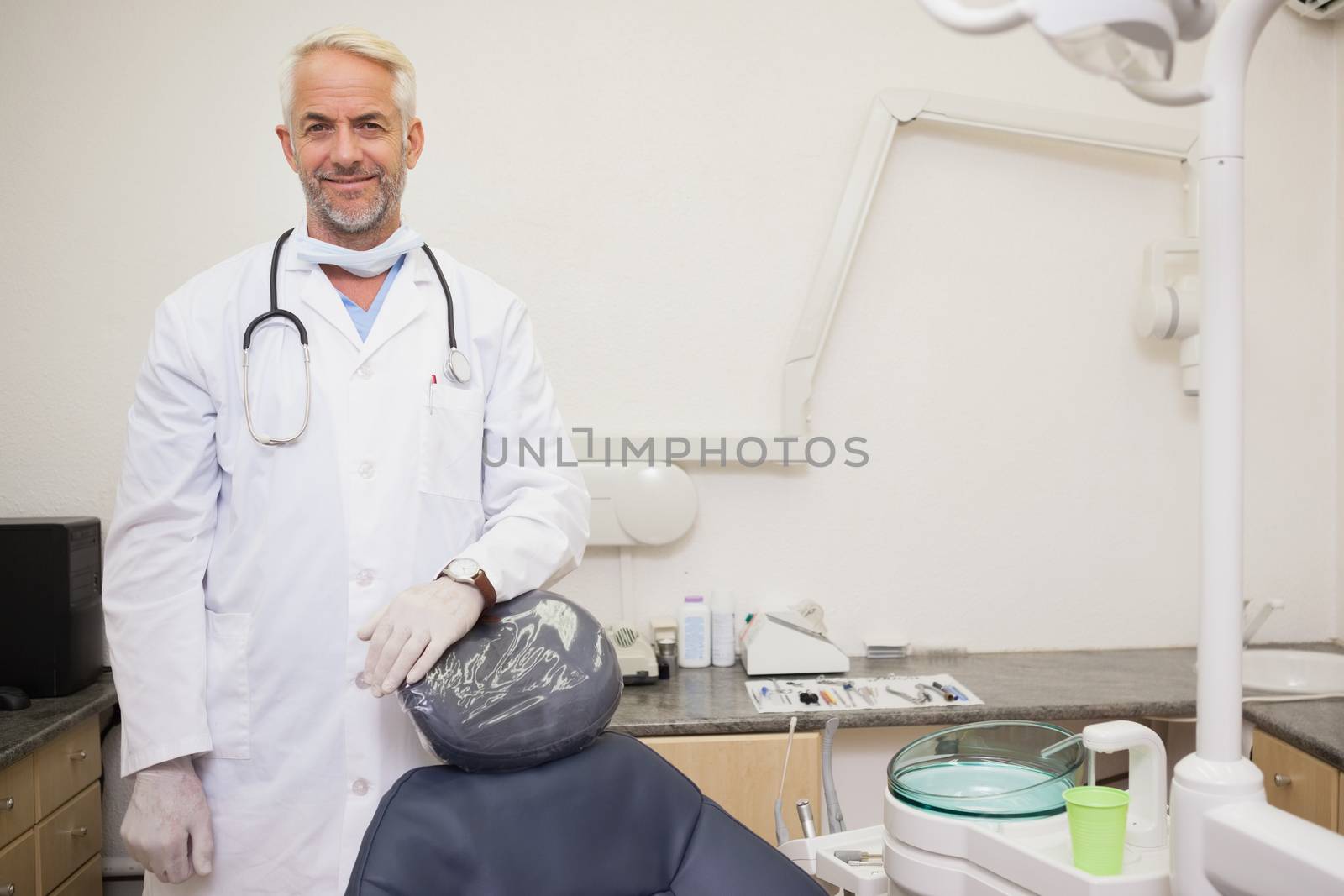 Dentist smiling at camera beside chair at the dental clinic