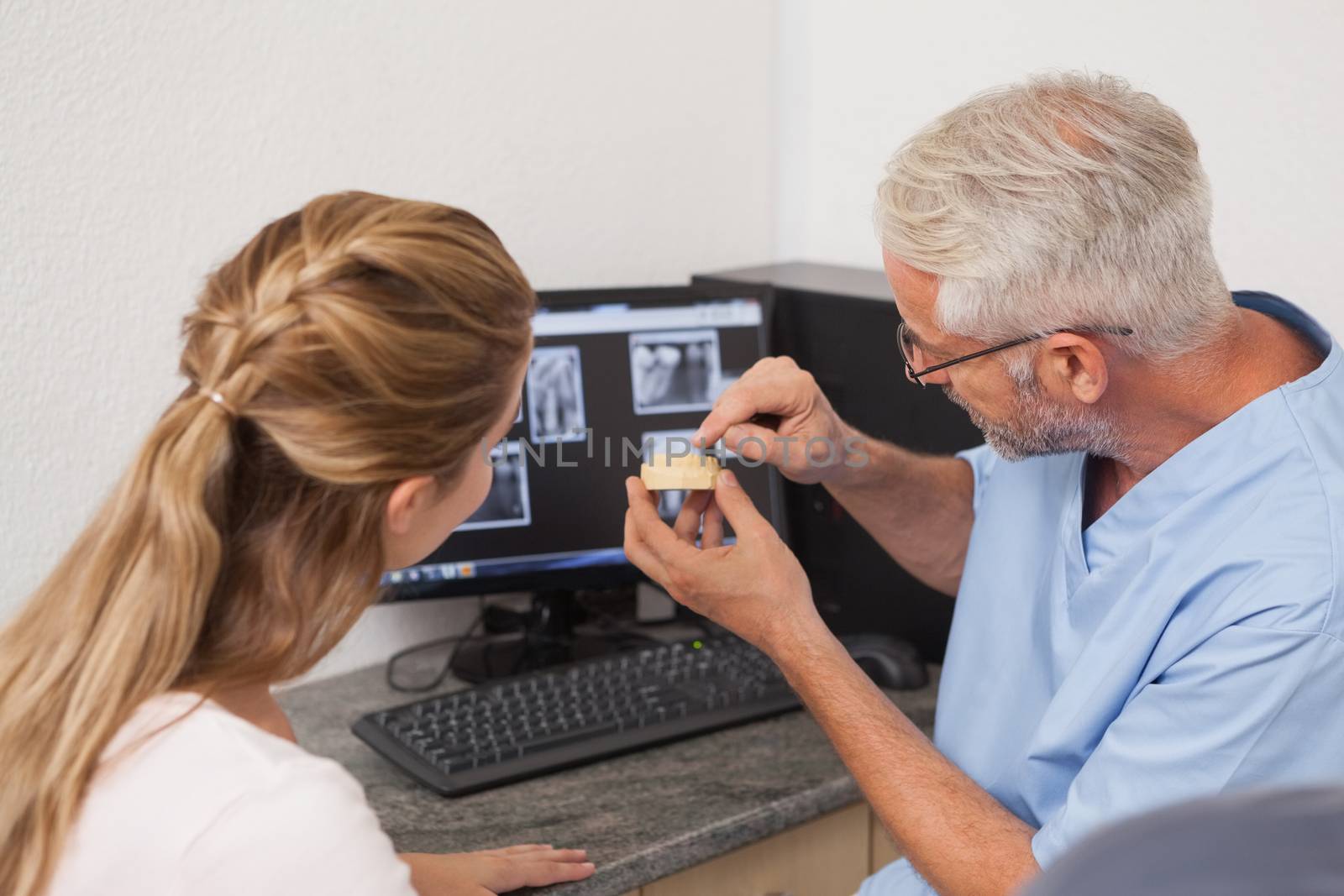 Dentist showing patient model of teeth and xrays by Wavebreakmedia