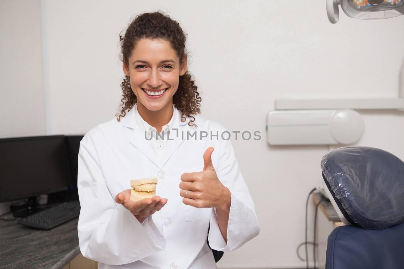Dentist showing thumbs up and holding mouth model at the dental clinic