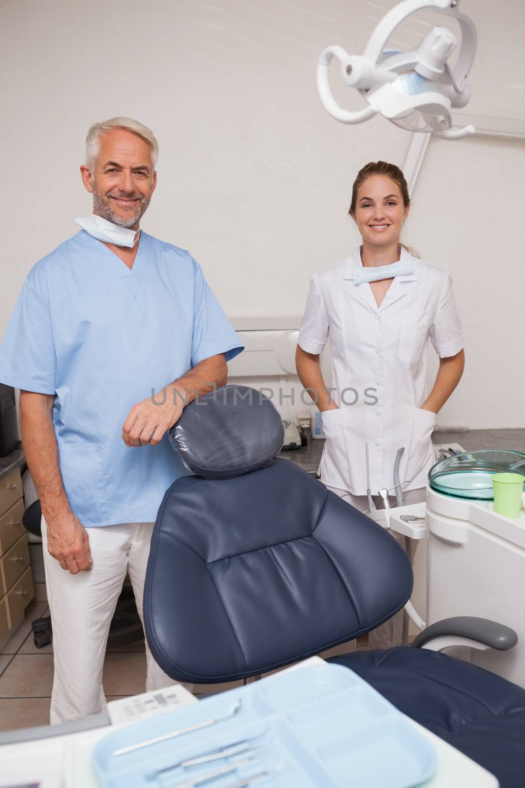 Dentist and assistant smiling at camera inviting you to the chair at the dental clinic