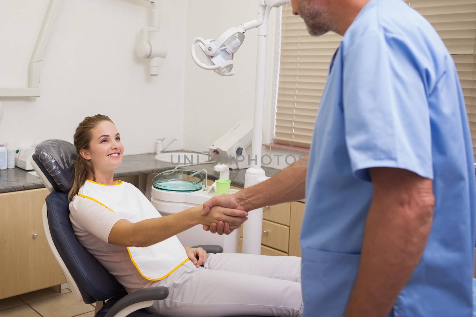 Dentist shaking hands with his patient in the chair at the dental clinic