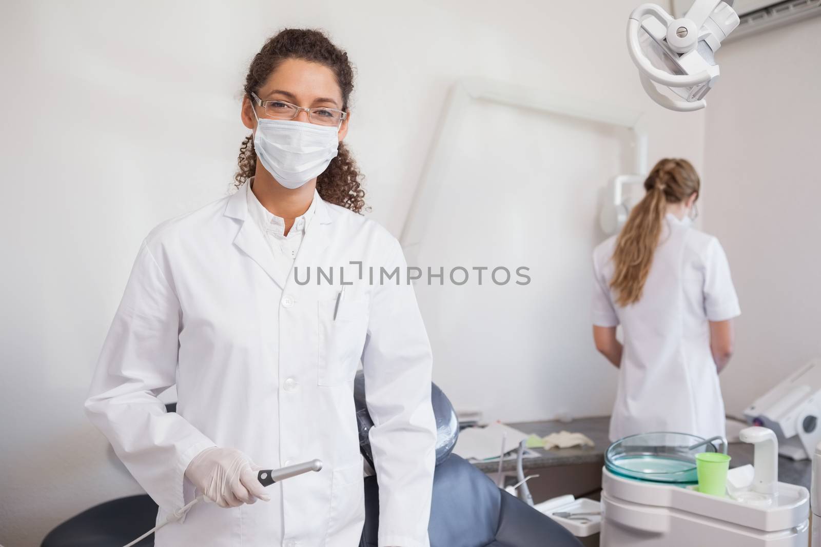 Dentist smiling at camera holding suction tube at the dental clinic