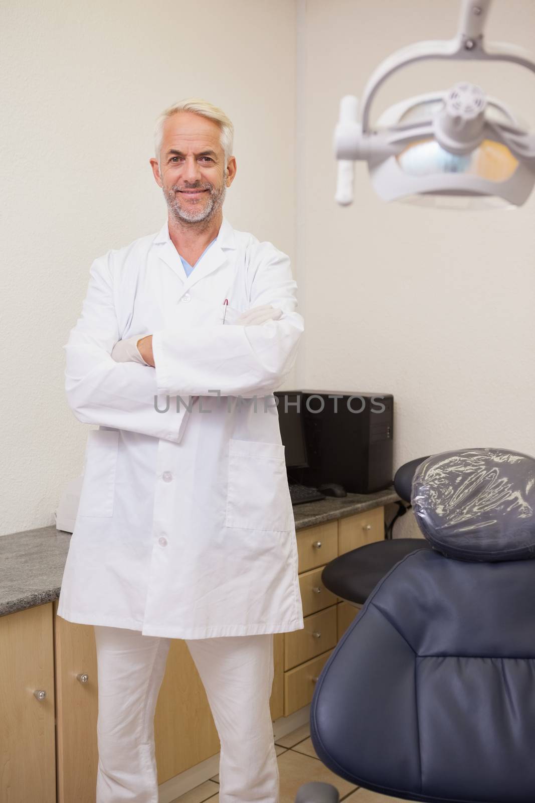 Dentist smiling at camera beside chair at the dental clinic