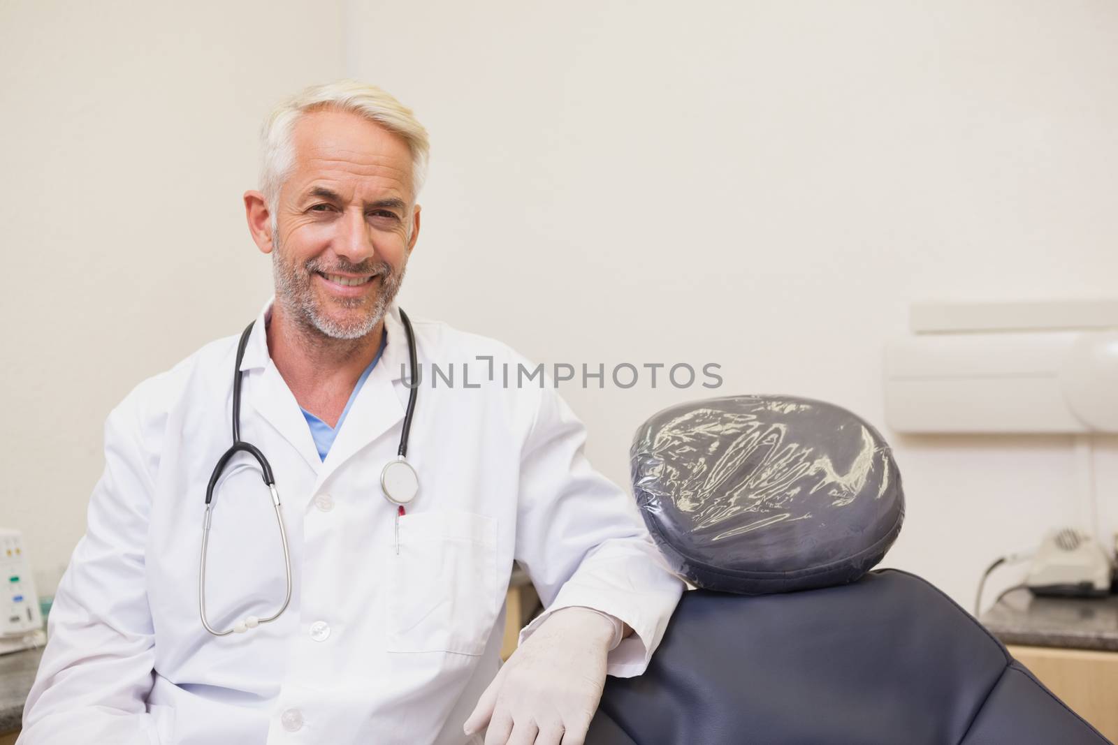 Dentist smiling at camera beside chair at the dental clinic