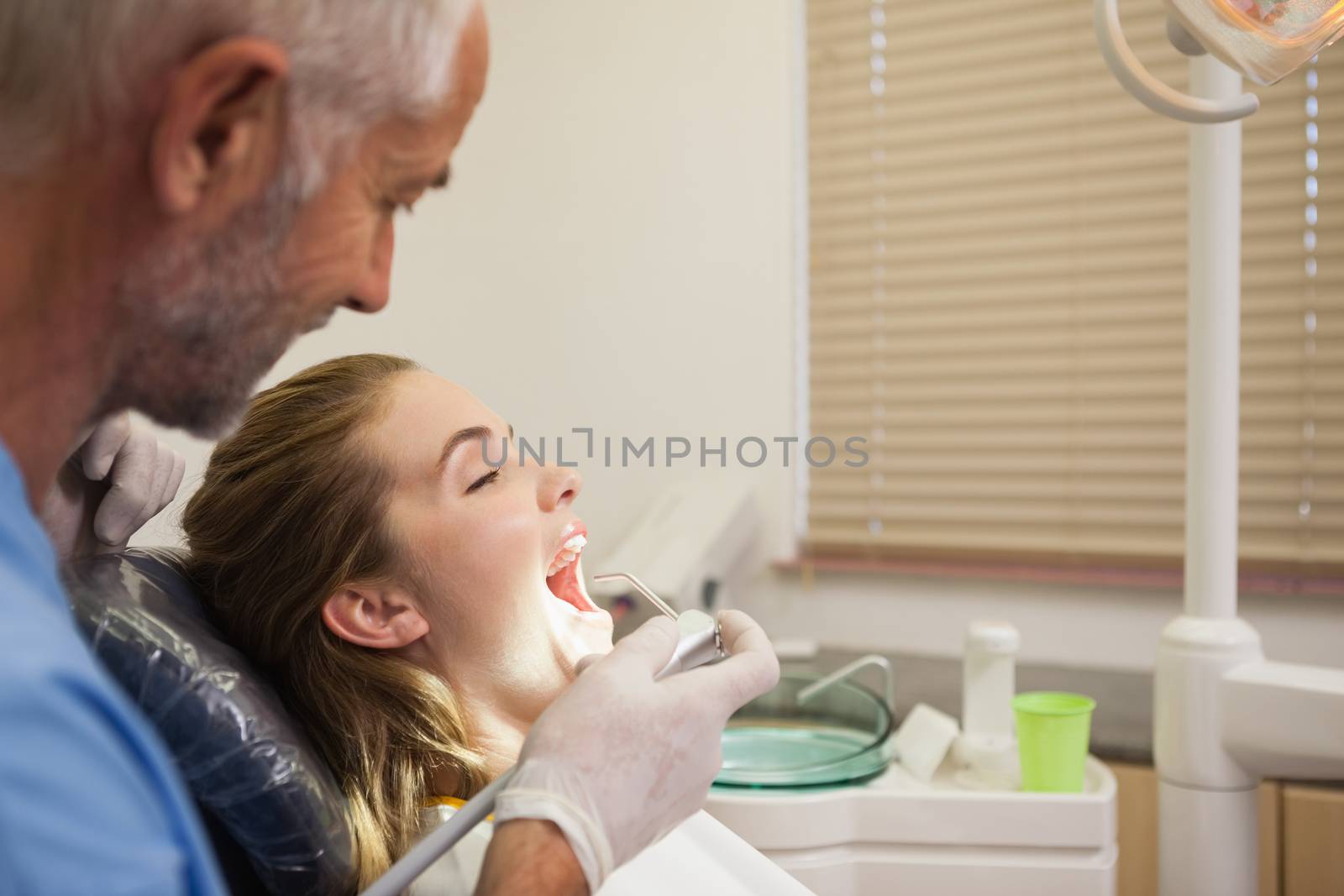 Dentist examining a patients teeth in the dentists chair under bright light at the dental clinic