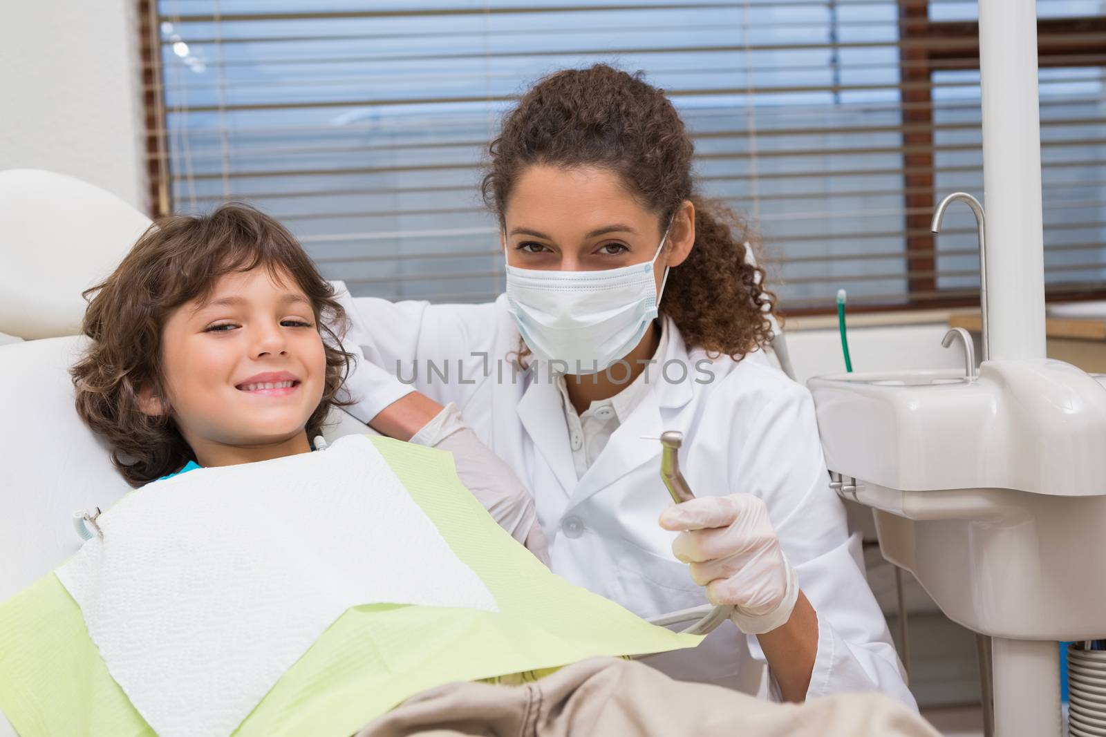 Pediatric dentist showing little boy in chair the drill at the dental clinic