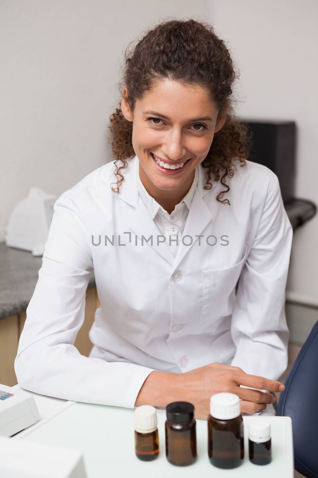 Dentist smiling at camera beside chair by Wavebreakmedia