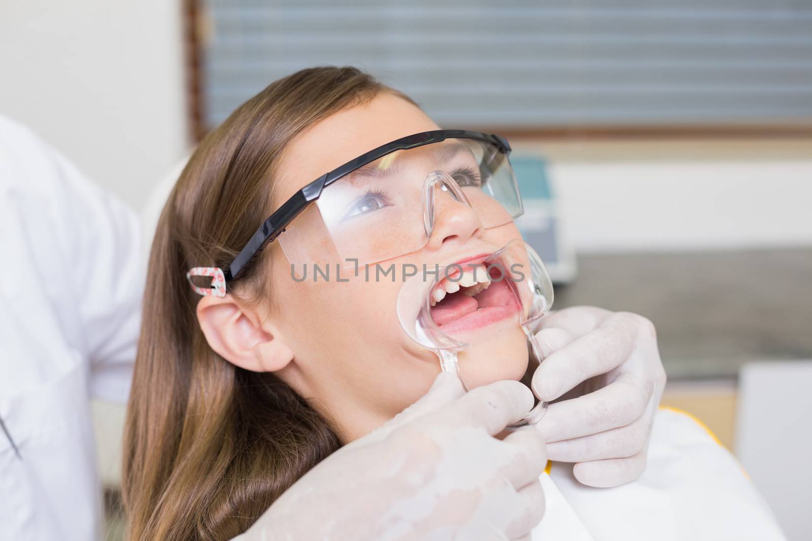Dentist putting mouth retractor on little girl at the dental clinic