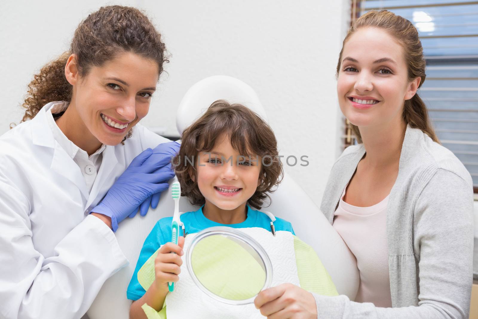 Pediatric dentist showing little boy how to brush teeth with his mother at the dental clinic