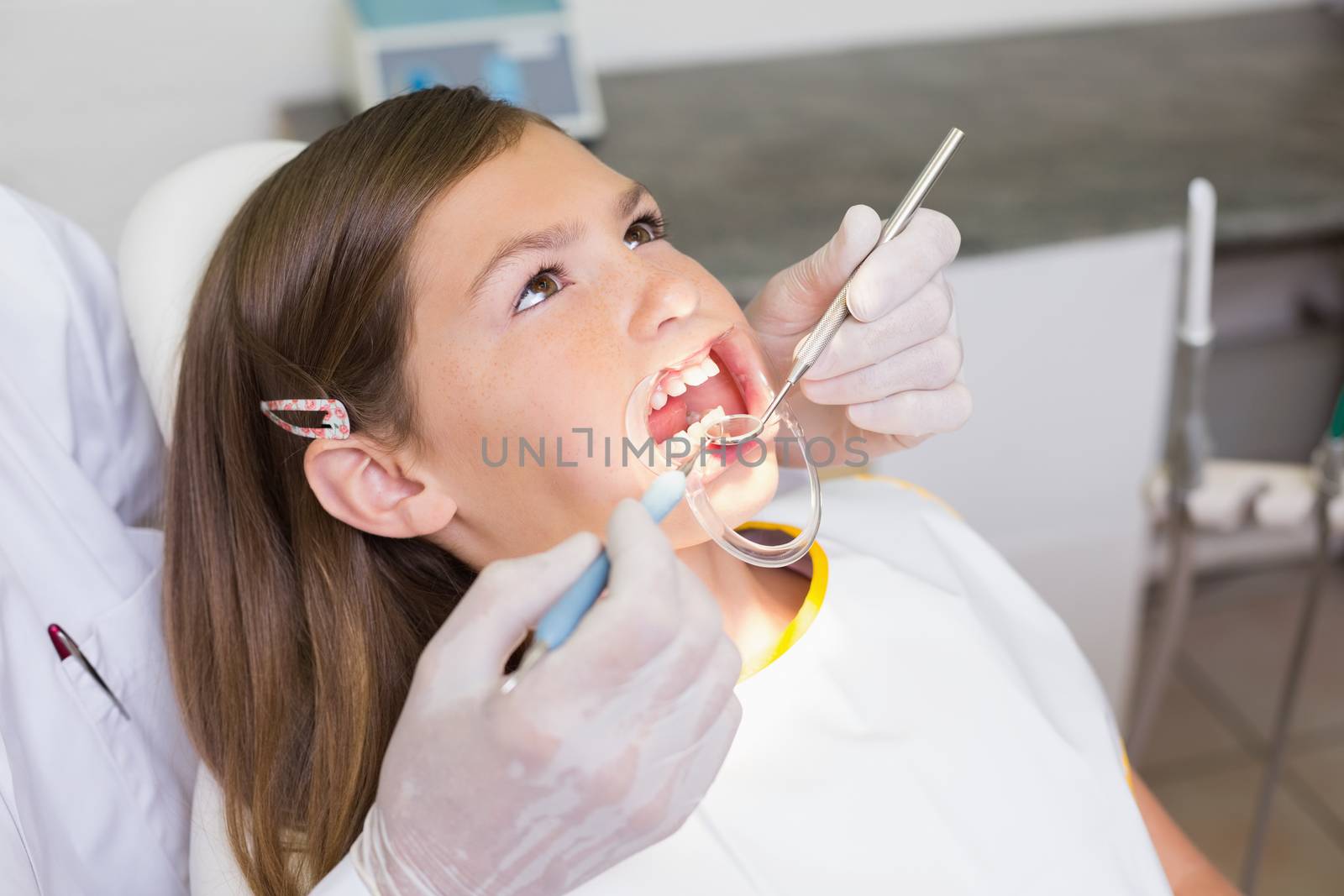 Dentist using mouth retractor on little girl at the dental clinic