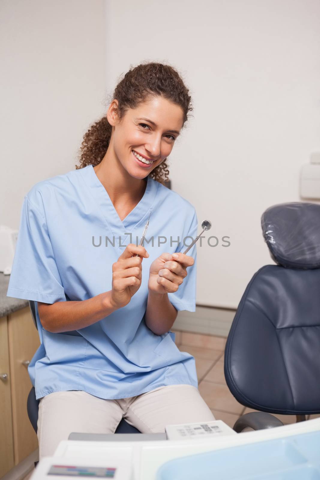 Dentist in blue scrubs smiling at camera holding tools at the dental clinic