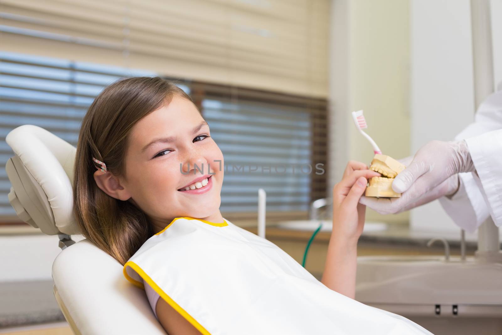 Pediatric dentist showing little girl teeth model at the dental clinic