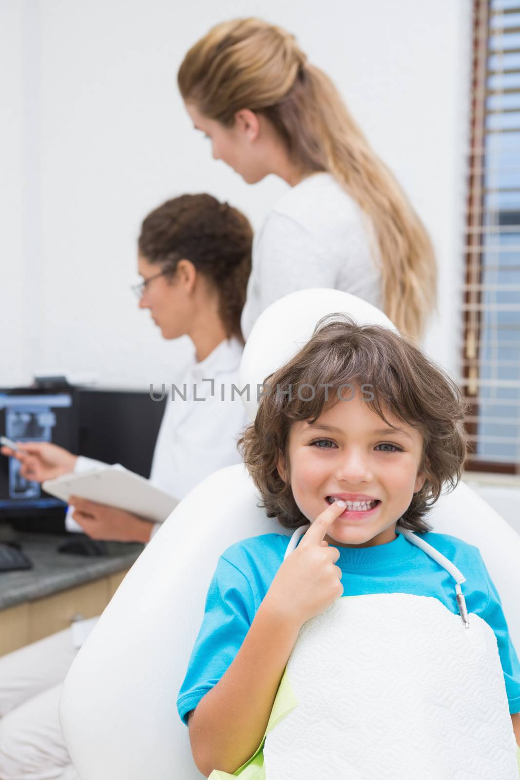 Little boy smiling at camera with mother and dentist in background by Wavebreakmedia