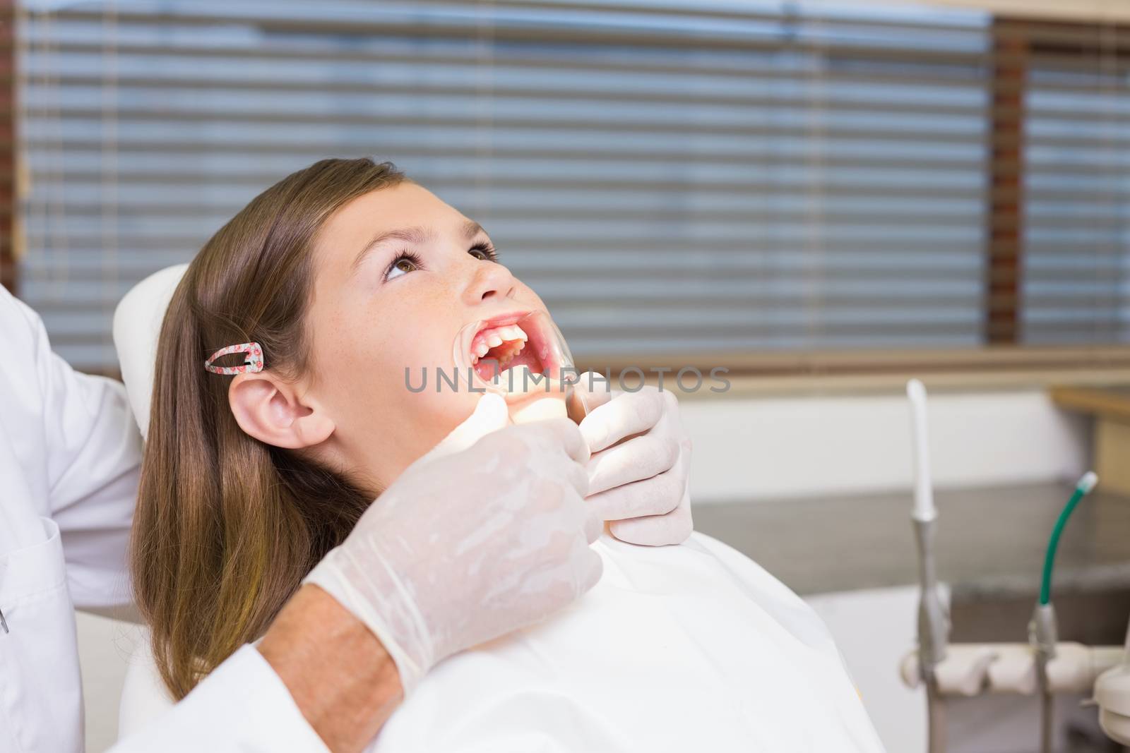 Dentist putting mouth retractor on little girl at the dental clinic
