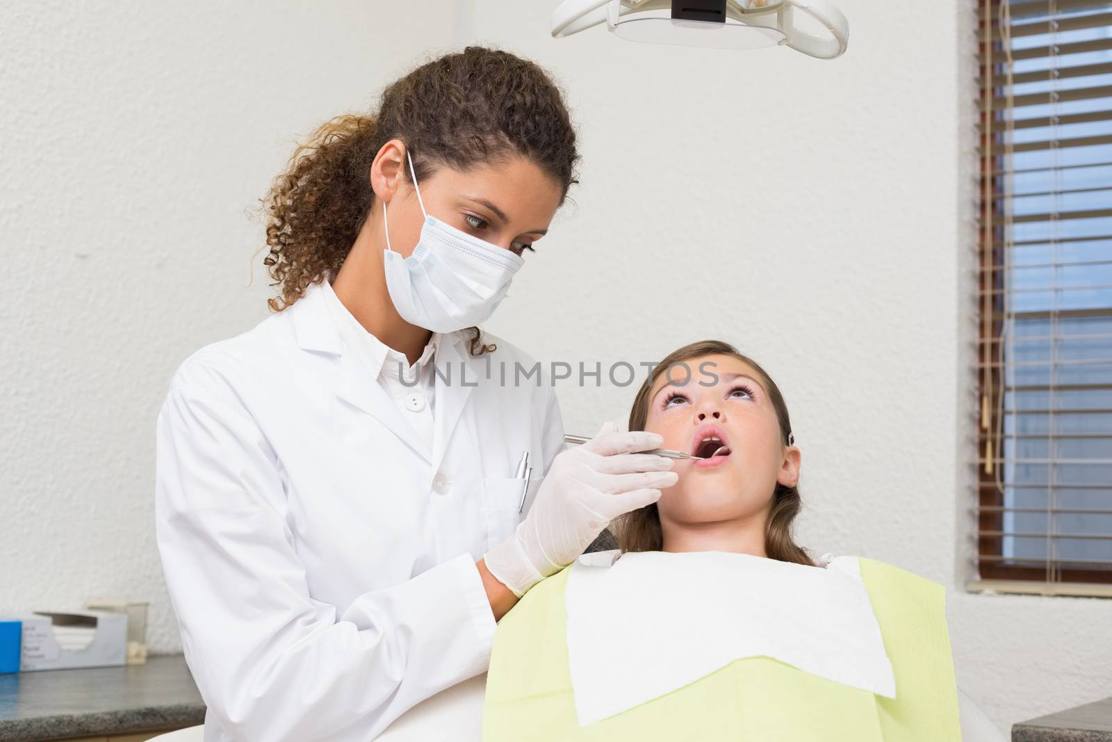 Pediatric dentist examining a patients teeth in the dentists chair at the dental clinic