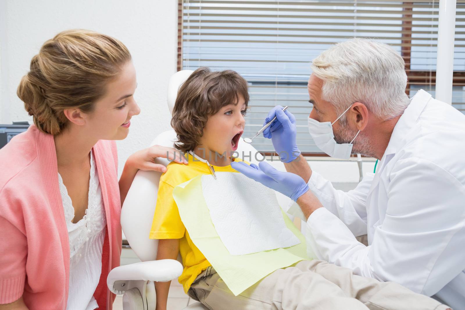 Pediatric dentist examining a little boys teeth with his mother watching  by Wavebreakmedia