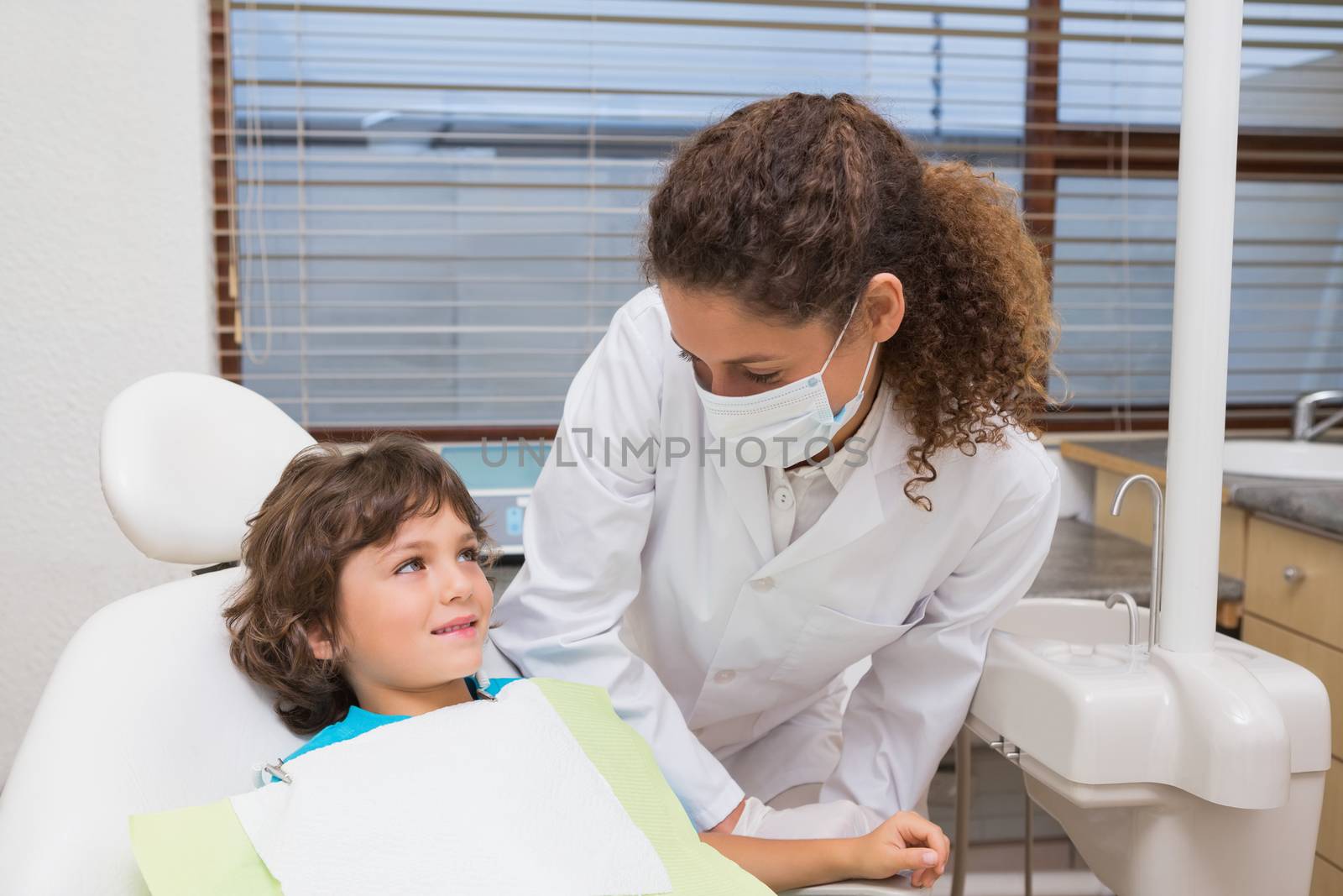Pediatric dentist smiling down at little boy in chair at the dental clinic
