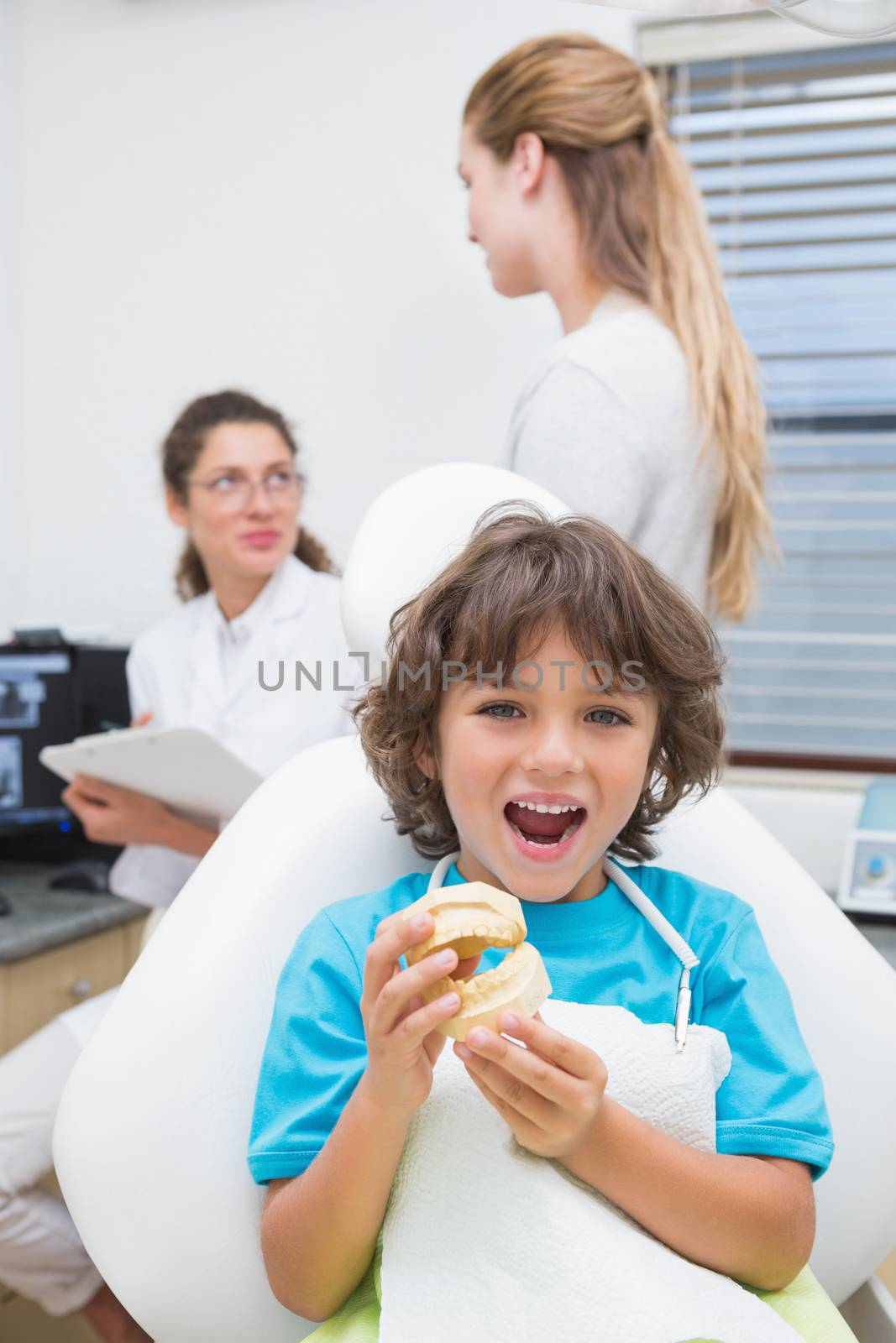 Little boy smiling at camera with mother and dentist in background by Wavebreakmedia