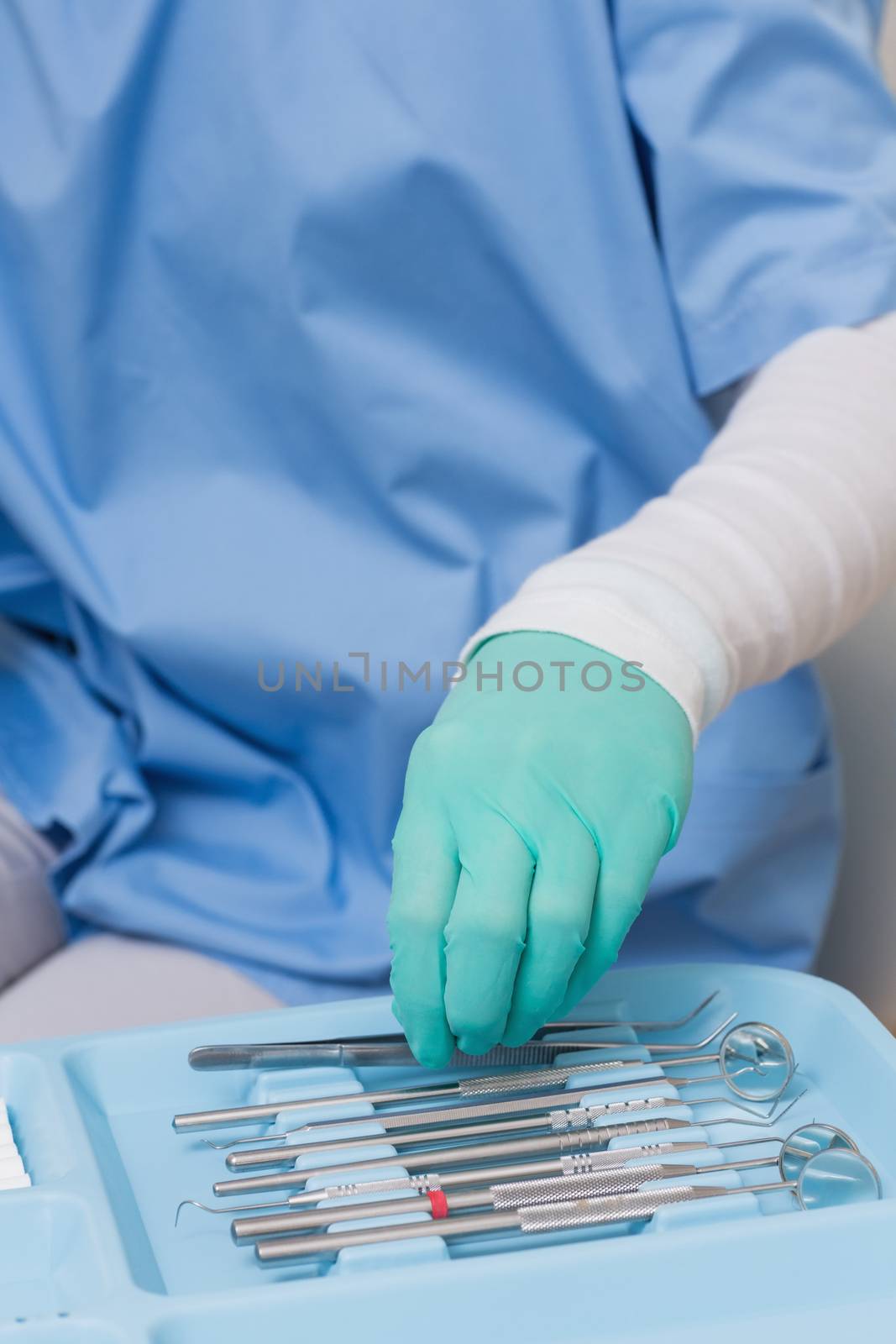 Dentist in blue scrubs picking up tools at the dental clinic