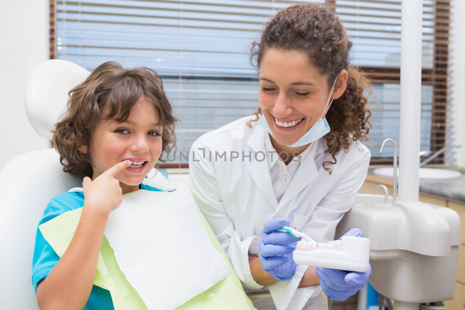 Pediatric dentist showing little boy how to brush his teeth at the dental clinic