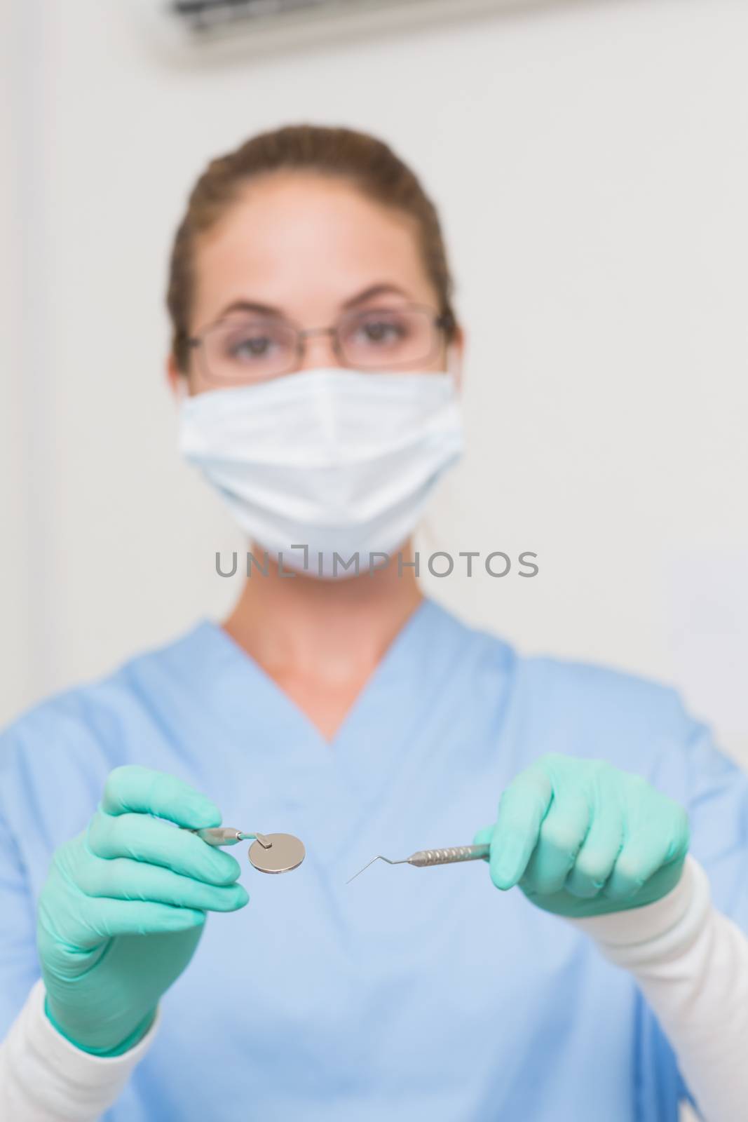 Dentist in blue scrubs holding tools looking at camera by Wavebreakmedia