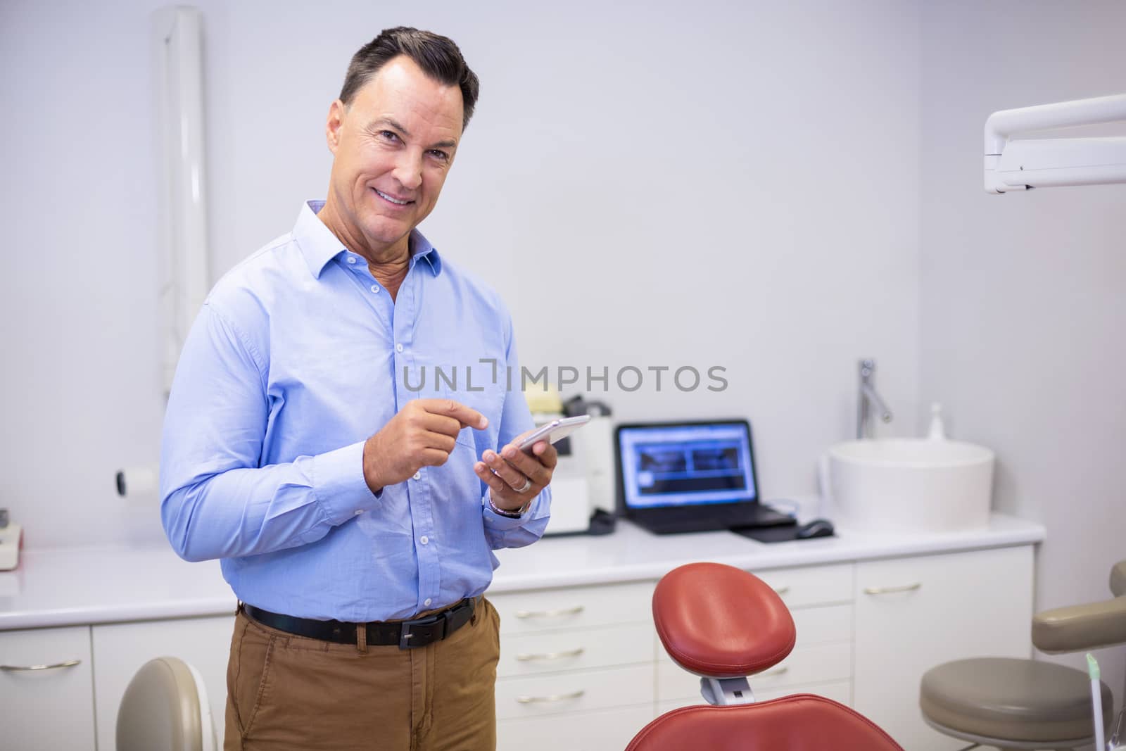 Portrait of smiling dentist using mobile phone in clinic