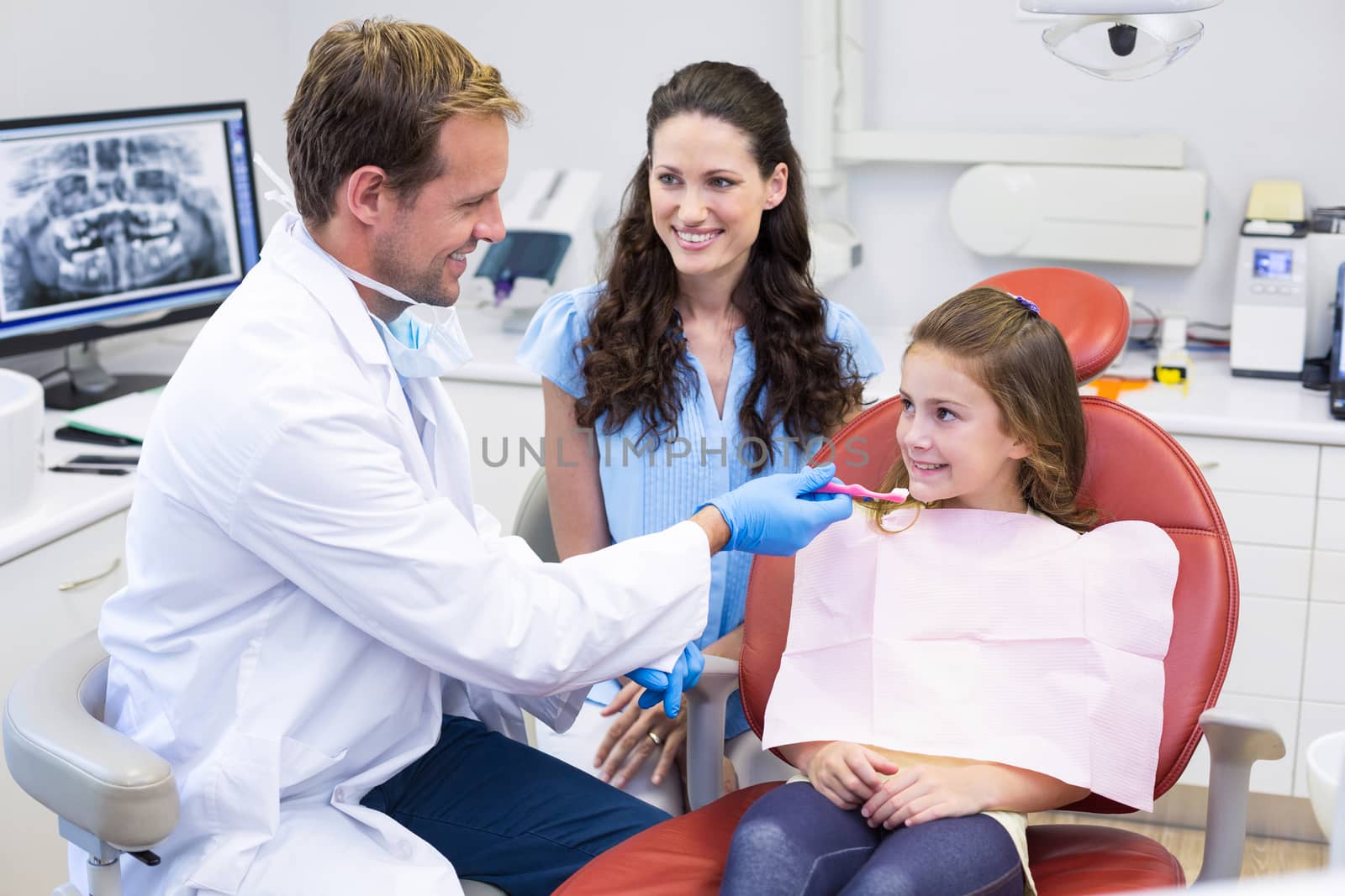 Dentist assisting young patient to brush teeth in dental clinic