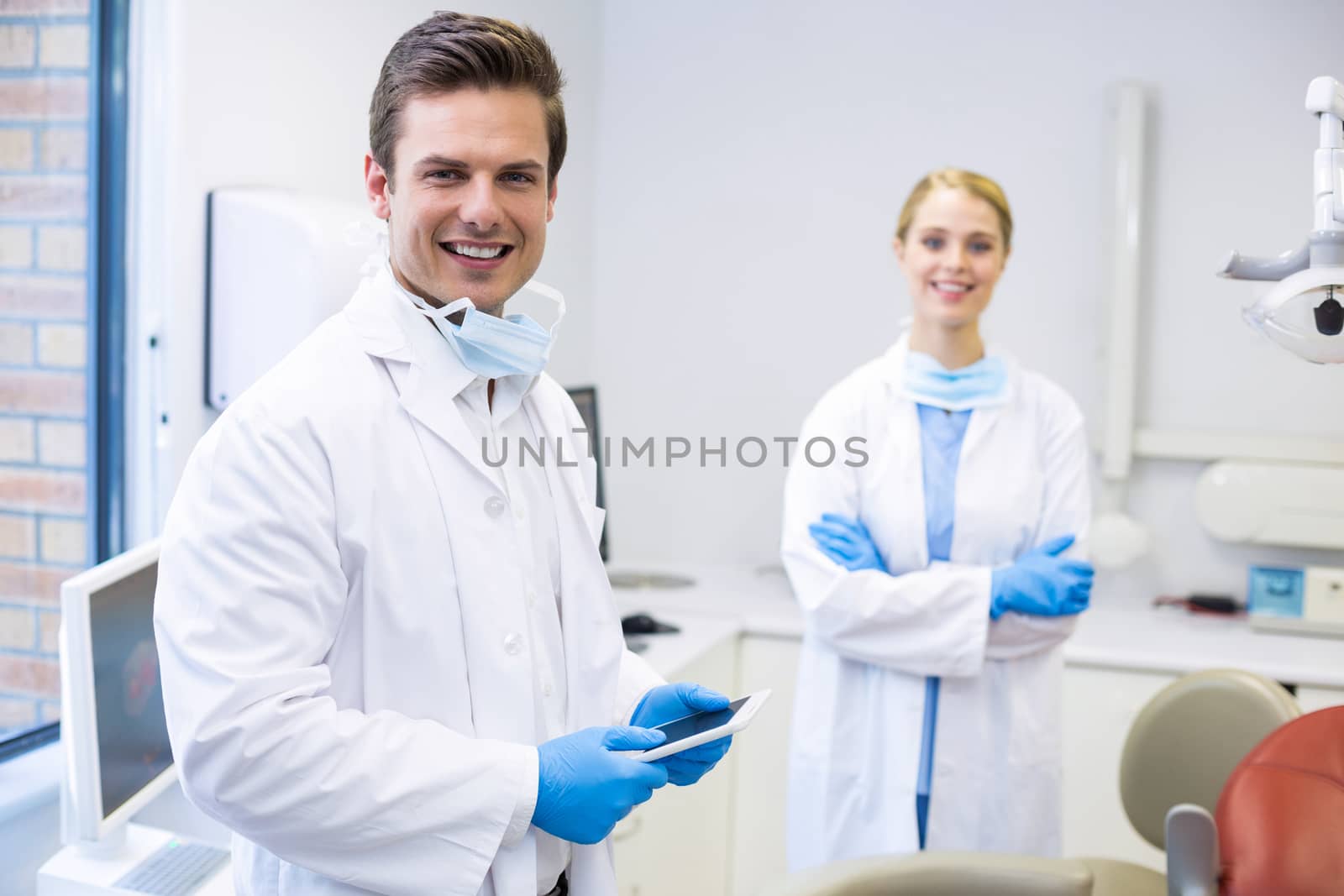 Portrait of dentist holding digital tablet while his colleague in background in clinic