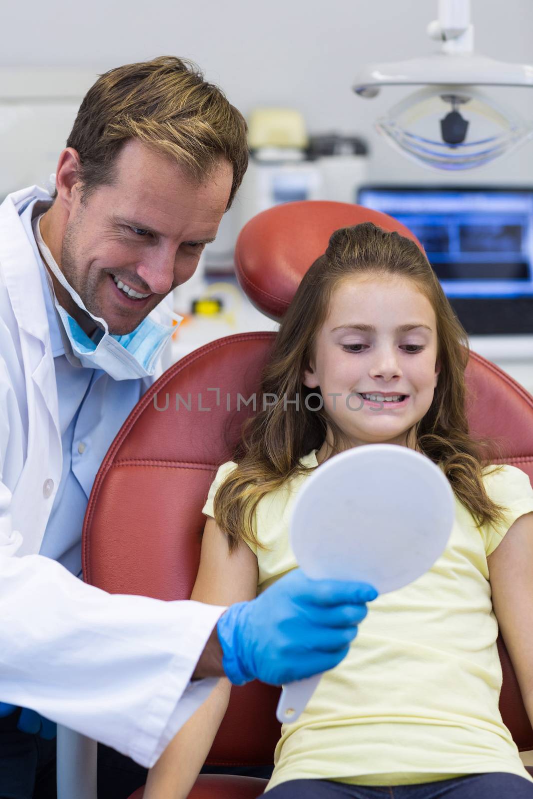 Dentist showing mirror to young patient in dental clinic by Wavebreakmedia