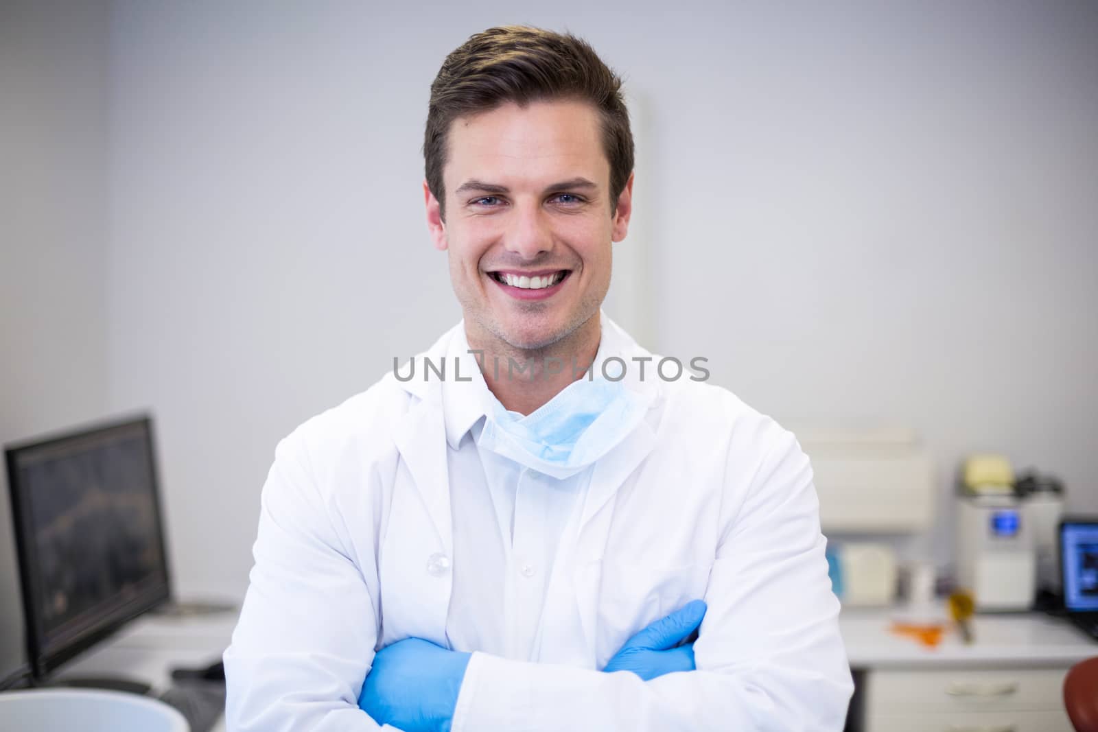 Portrait of happy dentist standing with arms crossed in clinic