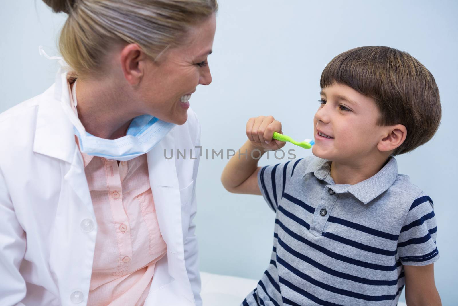 Boy holding toothbrush while looking at dentist by Wavebreakmedia