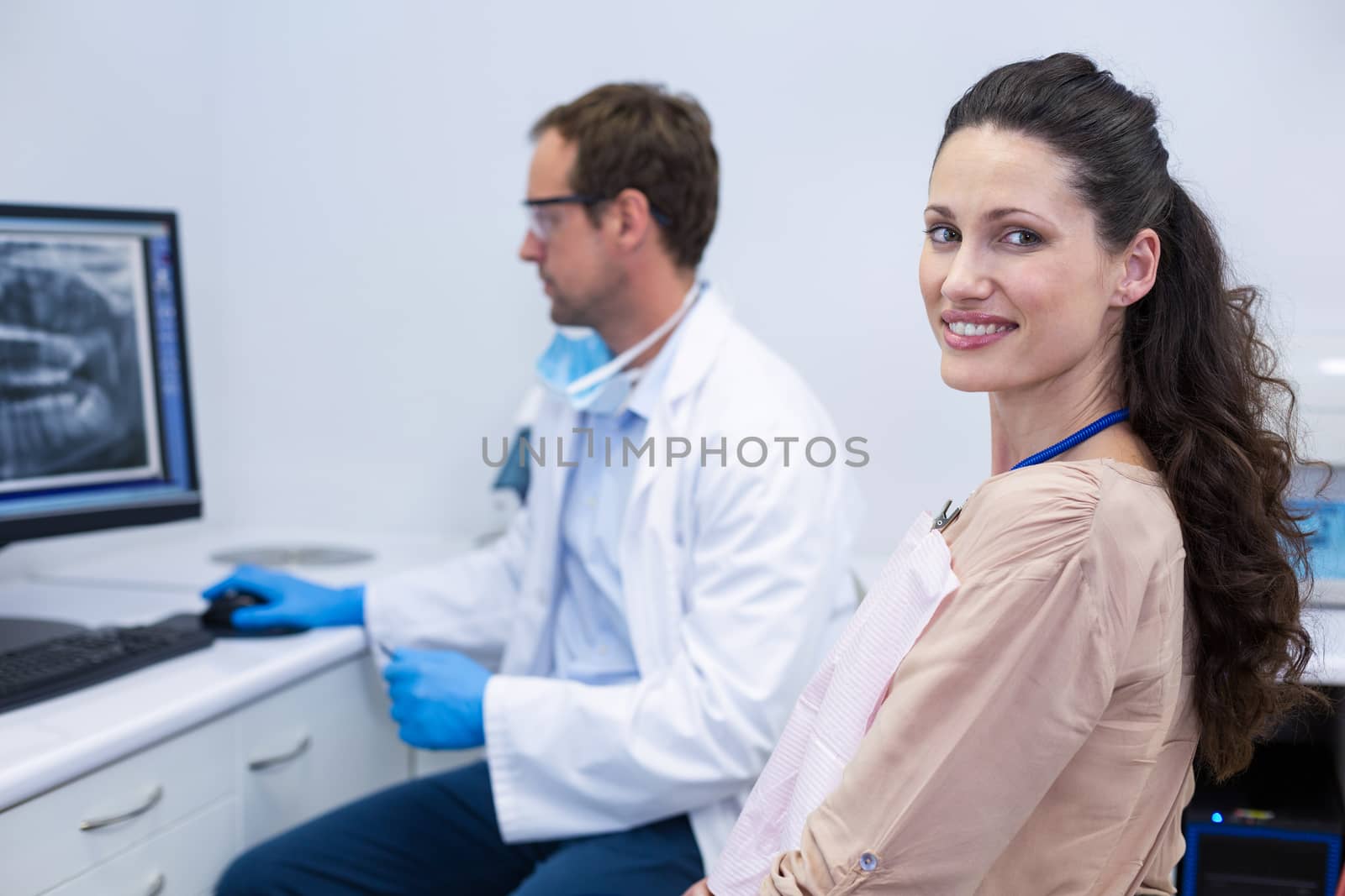 Female patient smiling at camera while dentist looking at an x-ray at dental clinic