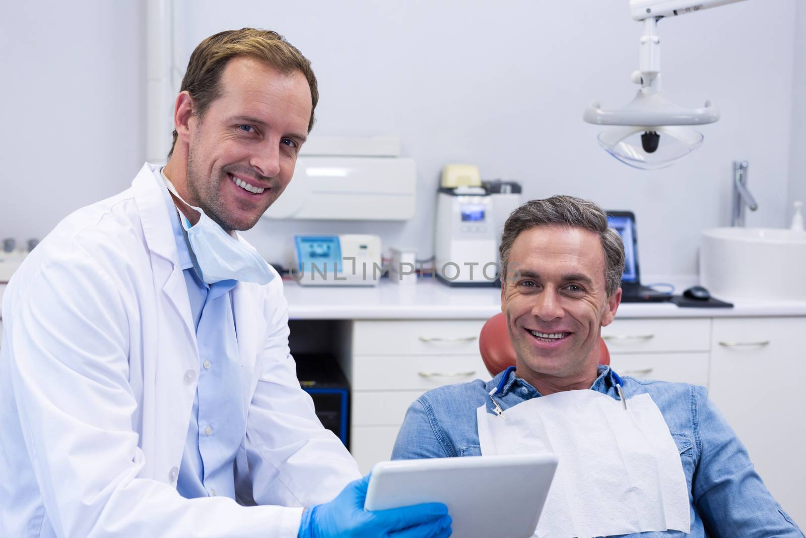 Dentist discussing over digital tablet with male patient by Wavebreakmedia