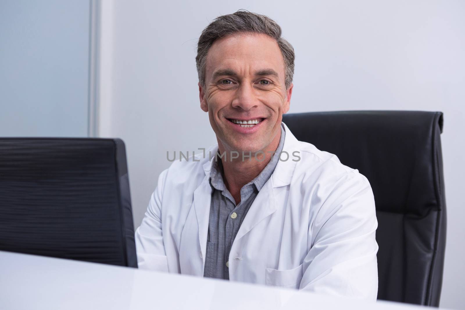 Portrait of dentist sitting by computer at table in clinic