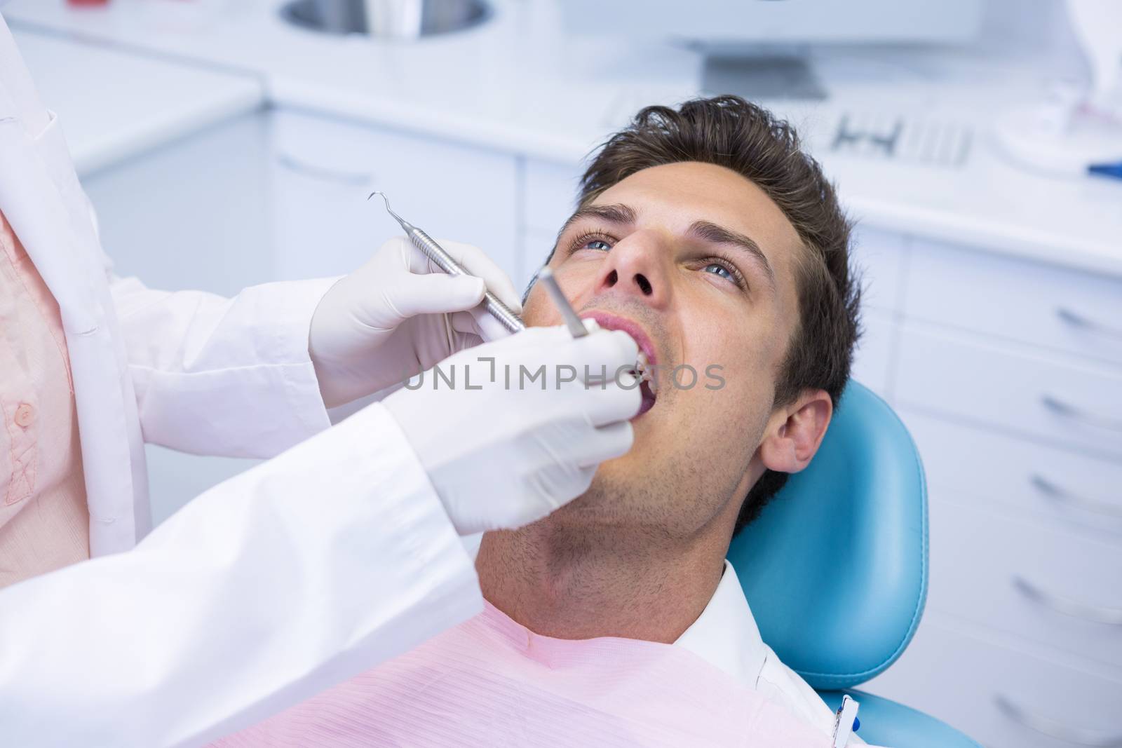 Dentist holding medical equipment while giving treatment to man at clinic