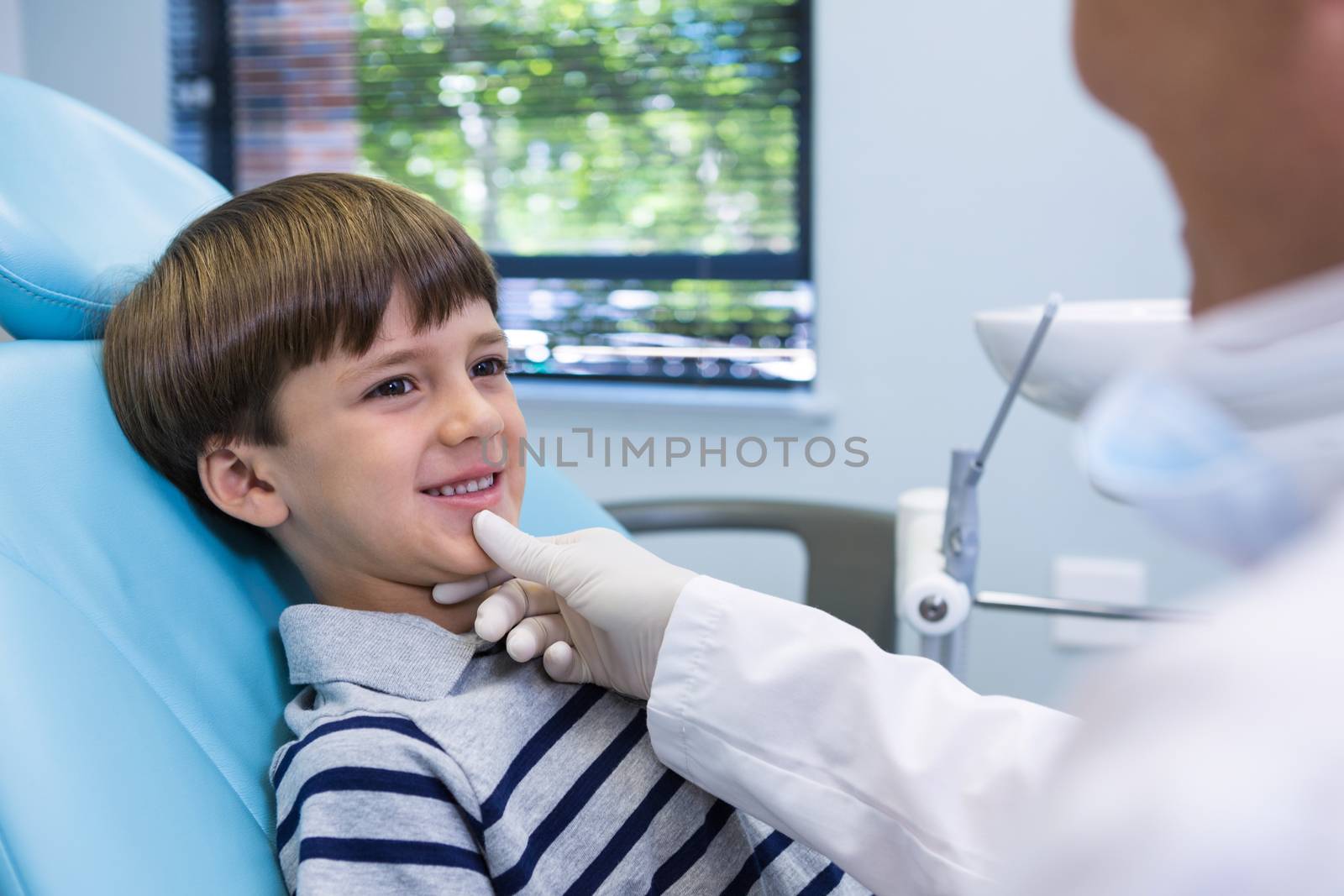 Smiling boy looking at dentist while sitting on chair by Wavebreakmedia