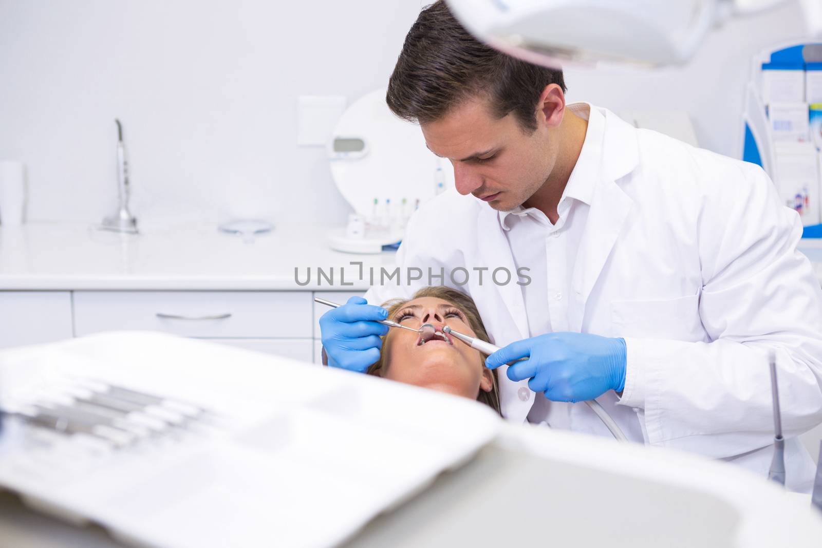 Dentist holding medical equipment while giving treatment to woman at clinic